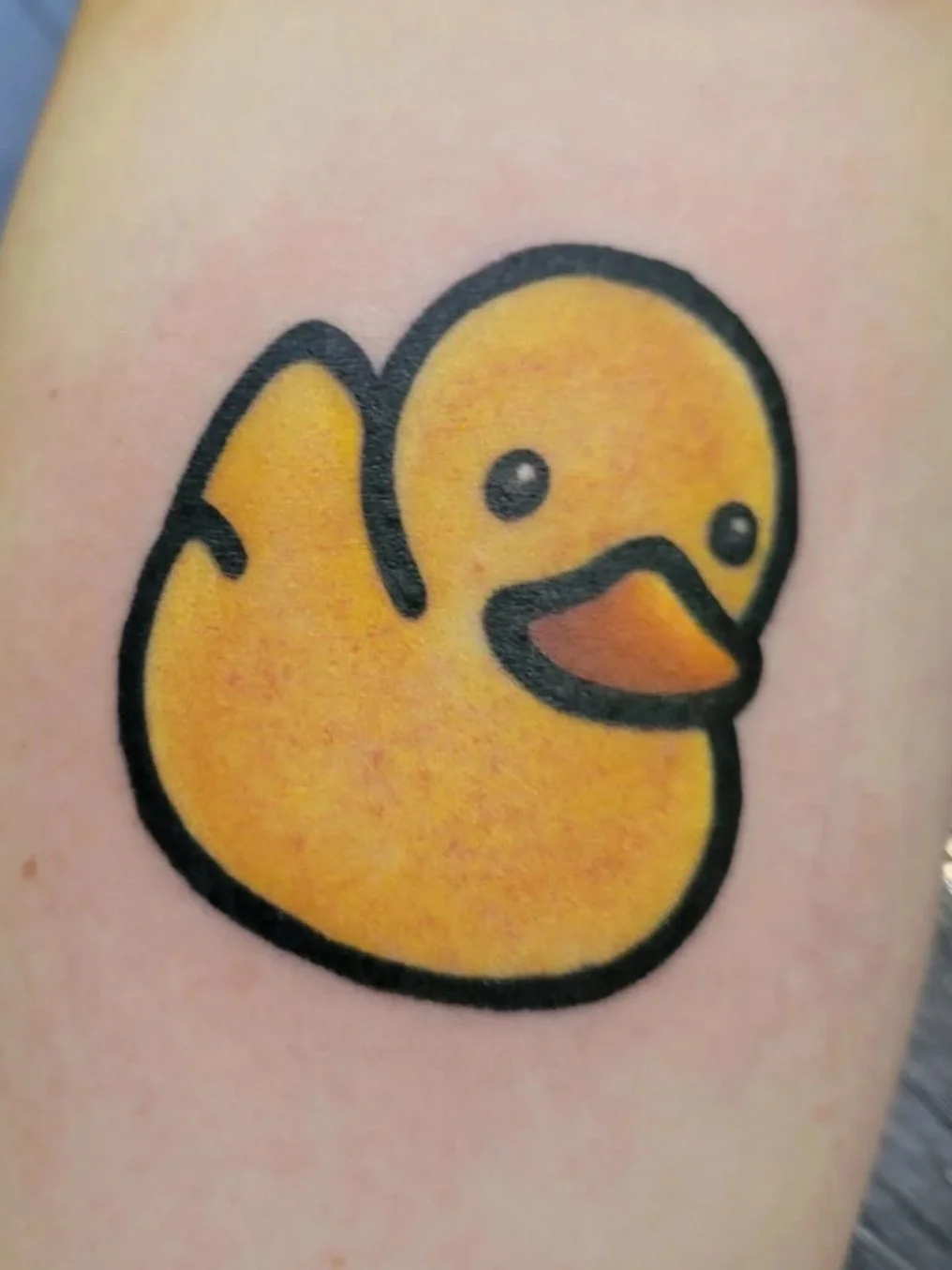 Tattoo of a cartoon yellow duck with a black outline and an orange beak.