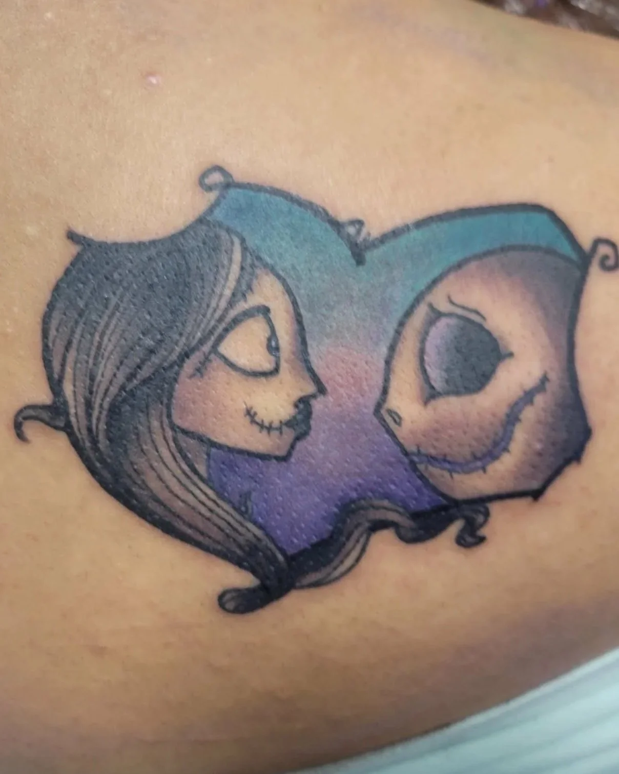 Tattoo of Nightmare Before Christmas characters Sally and Jack heads facing one another in a stylized heart frame.