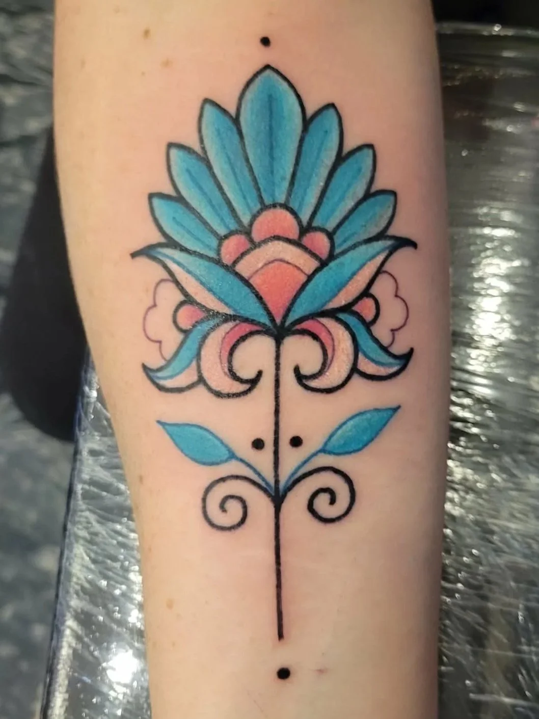 Colorful floral tattoo with blue petals, pink accents, and black outlines on a person's forearm.