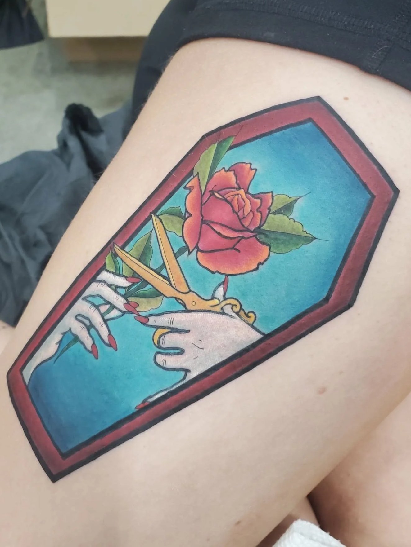 Tim Burton’s Wednesday inspired tattoo of hands cutting rose with scissors inside of a coffin