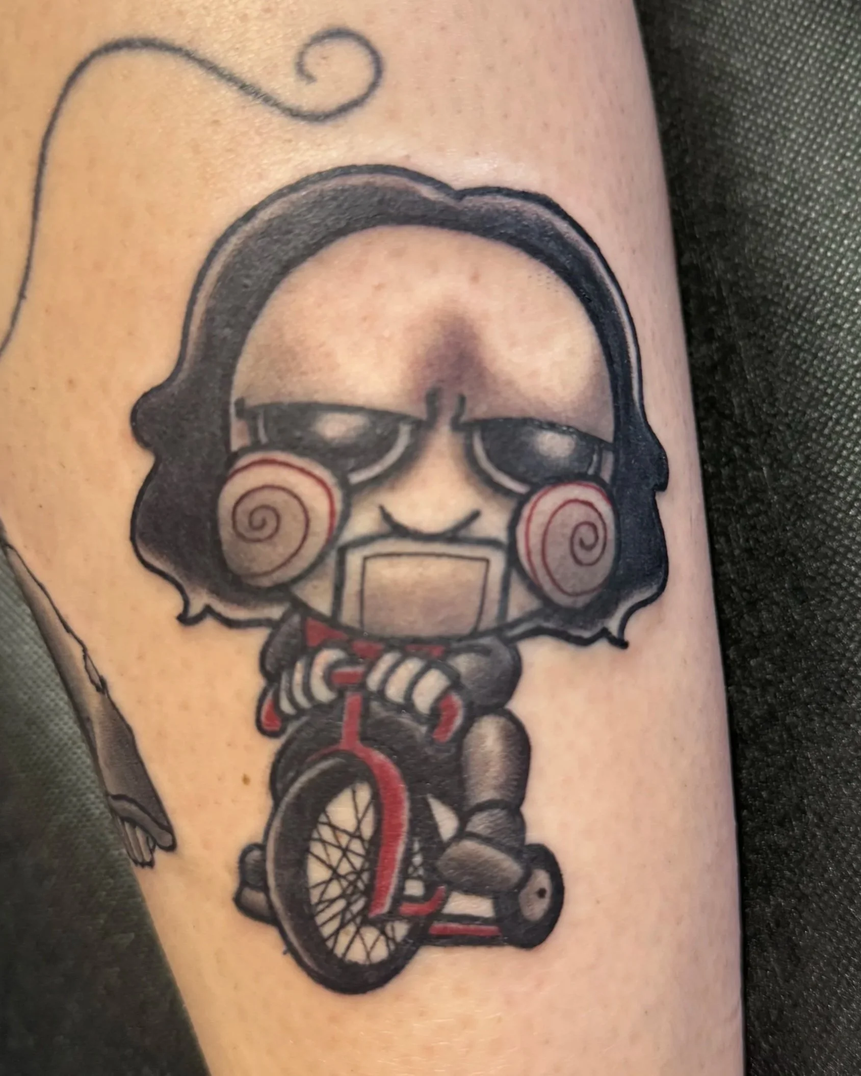 Tattoo of a person with curly hair, sunglasses, and lipstick, riding a tricycle.