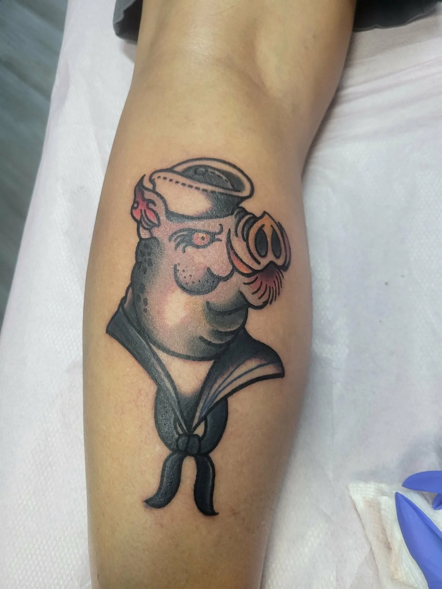 Tattoo of a pig with a sailor's hat and scarf, with the pig's face blending traditional tattoo style and a humorous pig face.