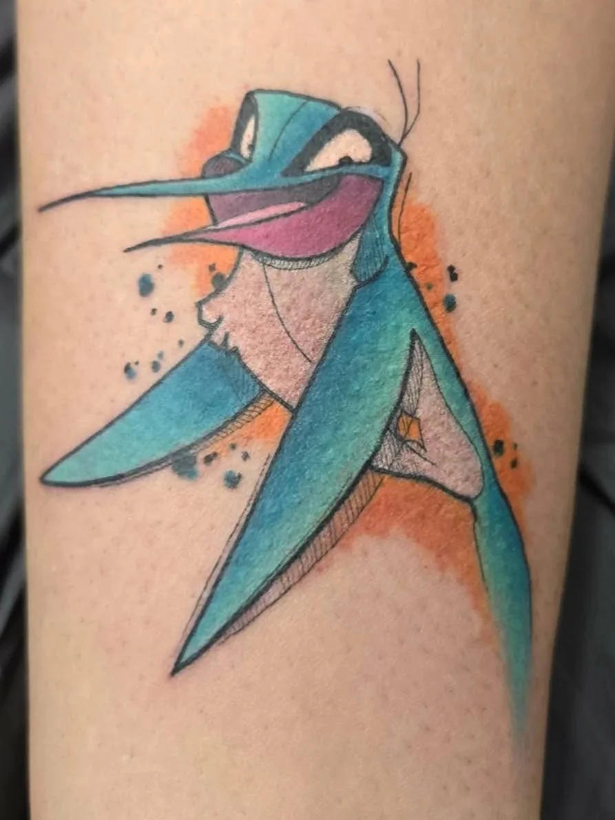 Colorful tattoo of a stylized hummingbird with a blue body, pink throat, and orange background on skin.