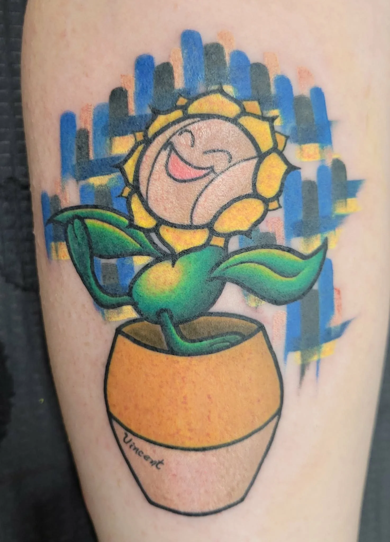 A colorful tattoo of a cartoon Pokemon with a smiling face, in a pot, with a vibrant blue and yellow background.