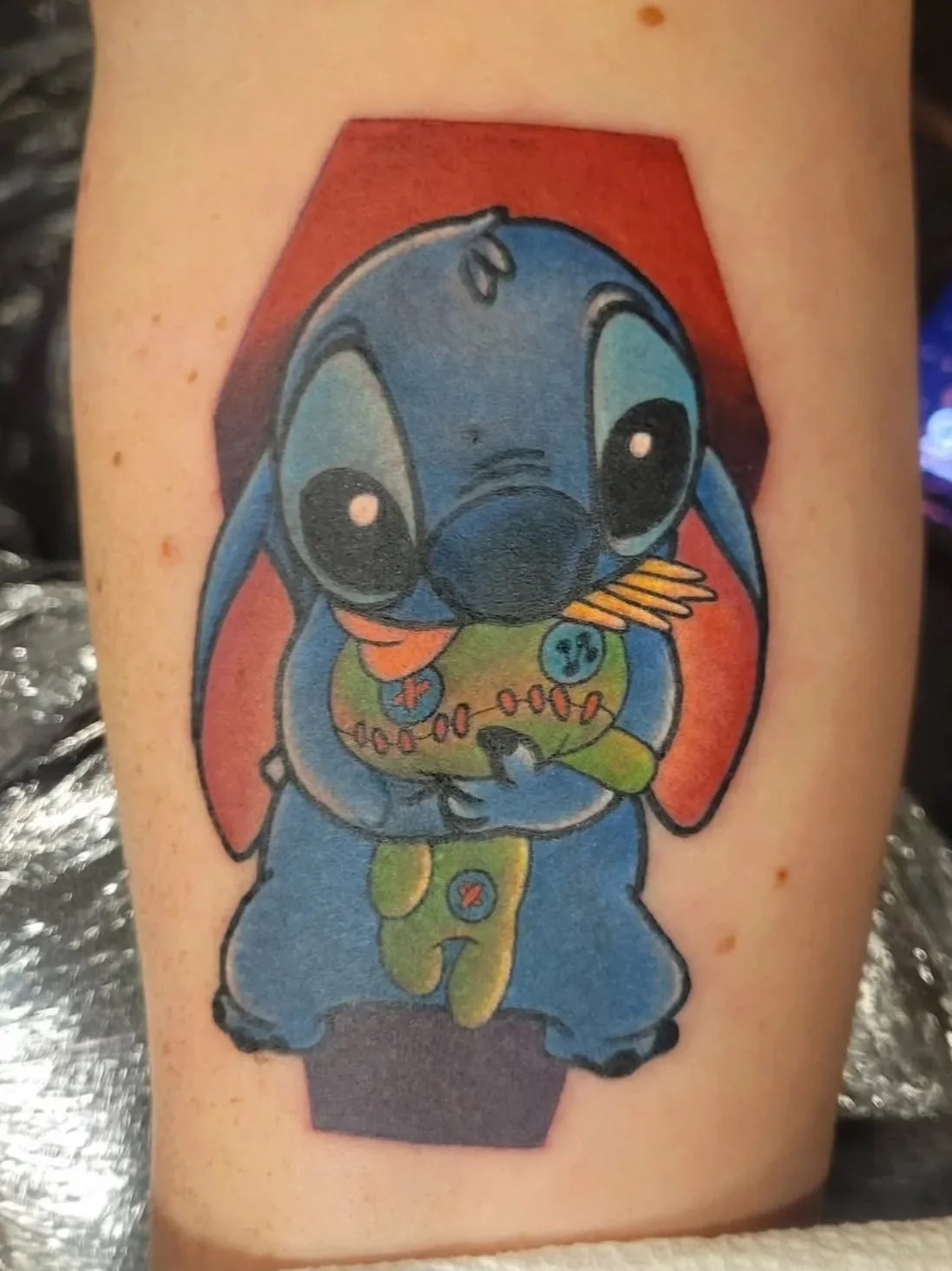 Colorful tattoo of Stitch from Disney's Lilo & Stitch holding Scrump doll.