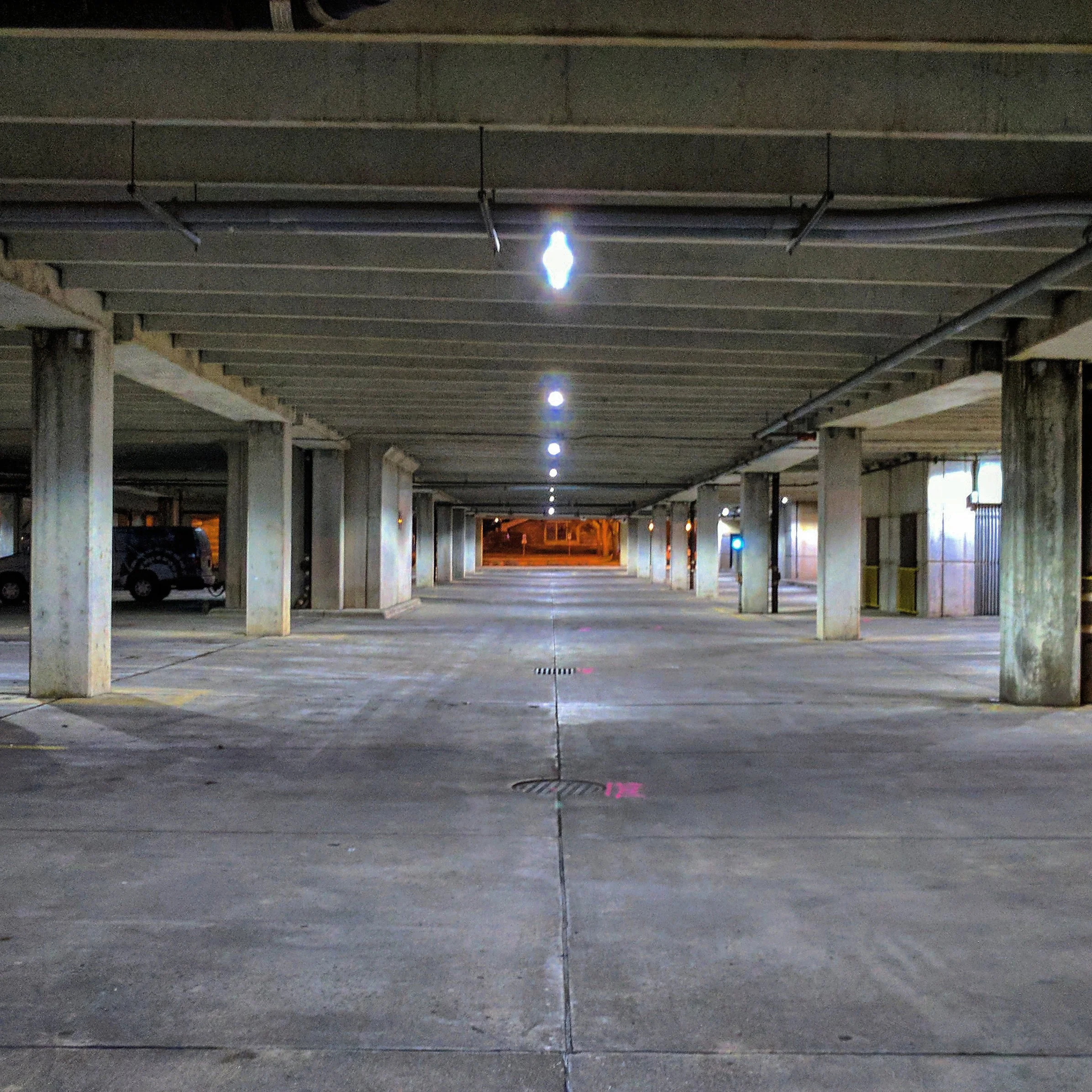 Underground parking garage with concrete pillars, overhead lighting, and parked cars to the sides.