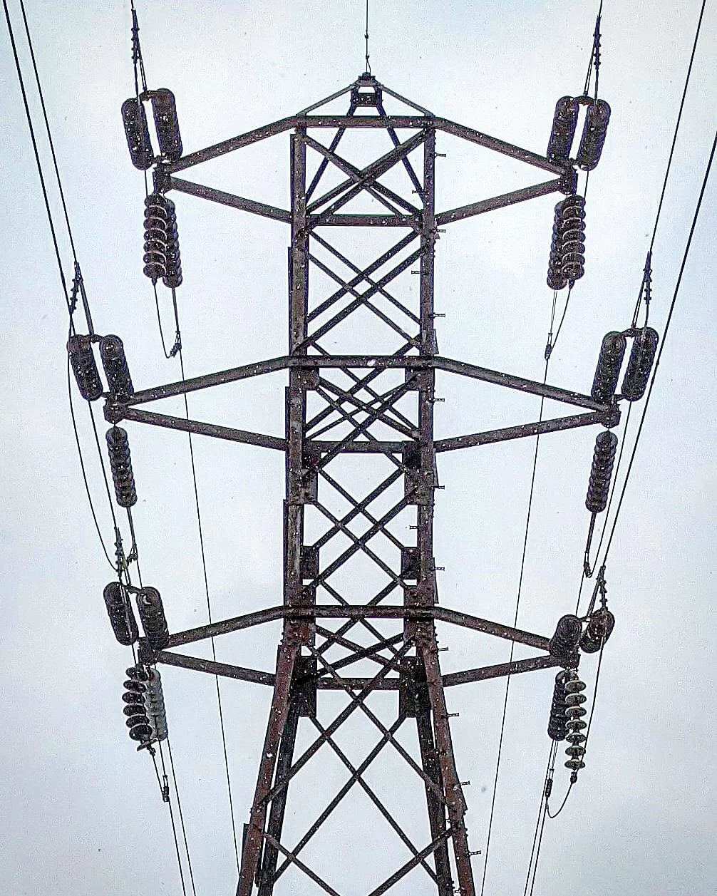A tall electrical transmission tower with multiple power lines extending from it against a cloudy sky.