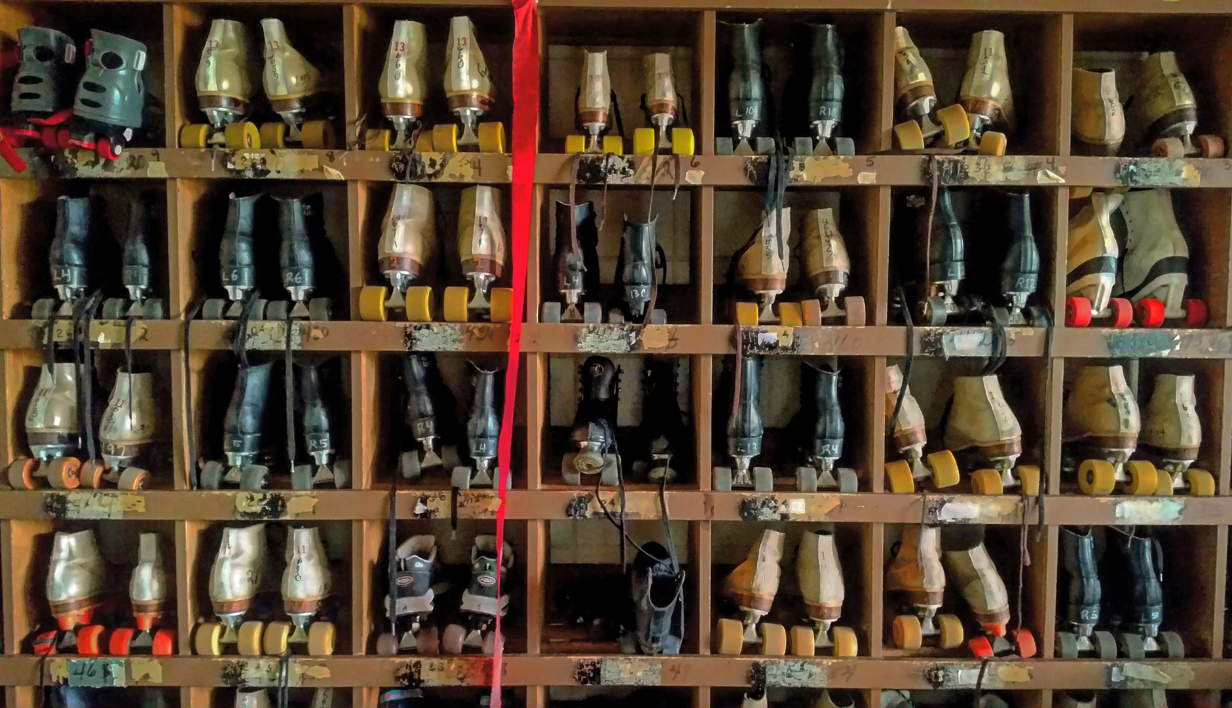 A wall of various skate or rollerblades stored in wooden cubbies, organized by size and style.