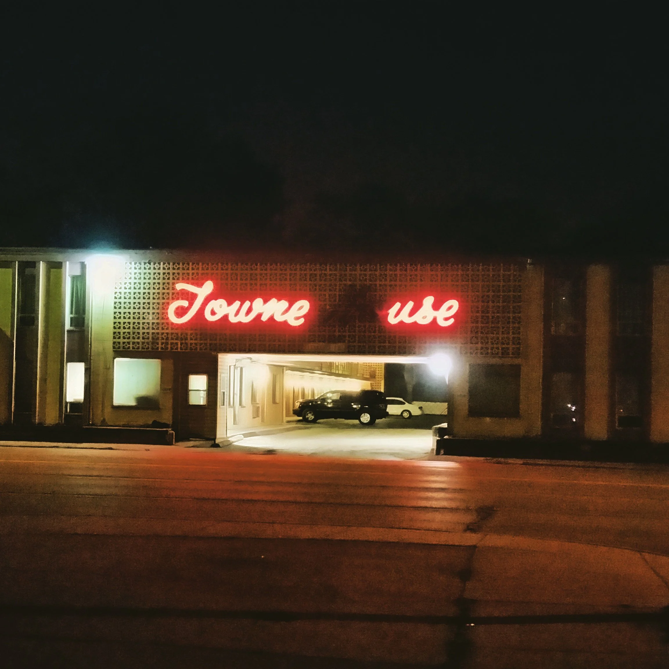 Night view of a building with a neon sign reading 'Town use,' with a parking area and cars underneath, illuminated by exterior lighting.