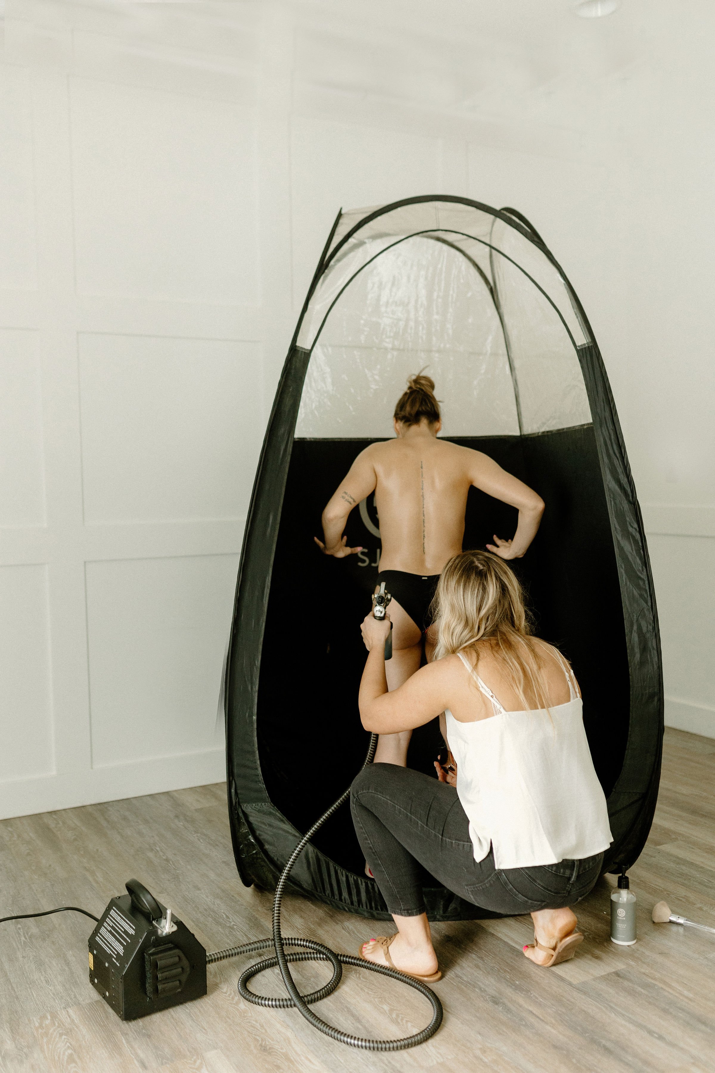 A woman is taking a photo of a man inside a photo booth, who is standing with his back to the camera.