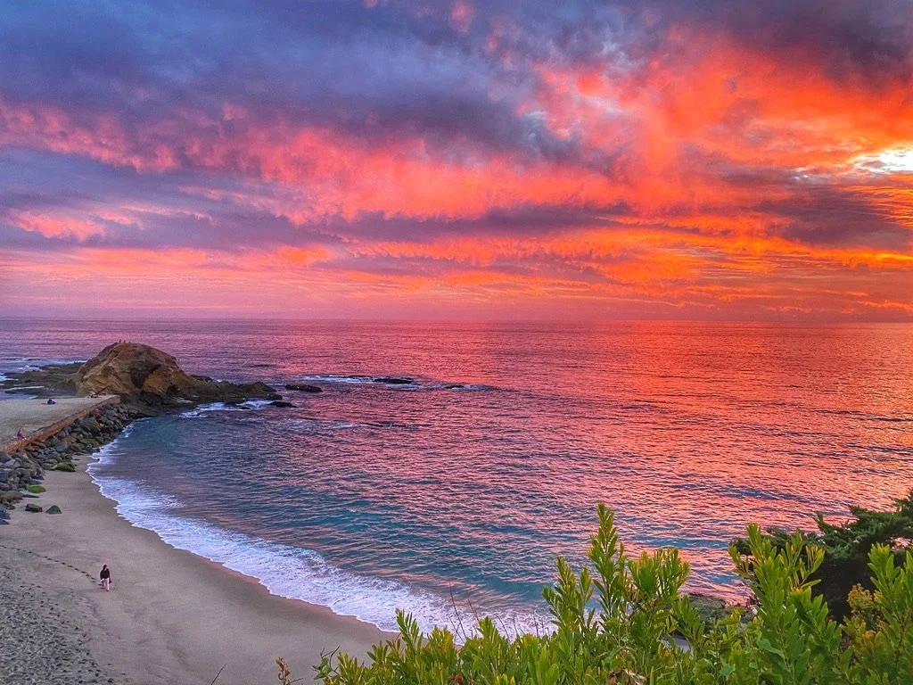 a view of sunset overlooking a beach with turquoise water and bright orange pink clouds in Laguna Beach California