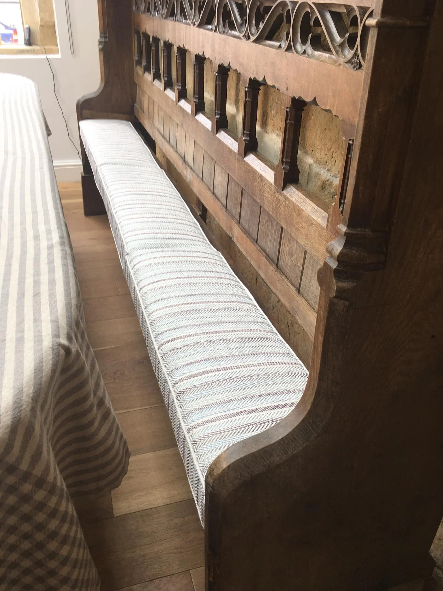 A wooden bench with a striped cushion placed against a wall and next to a striped fabric-covered piece of furniture, with a wooden floor underneath.