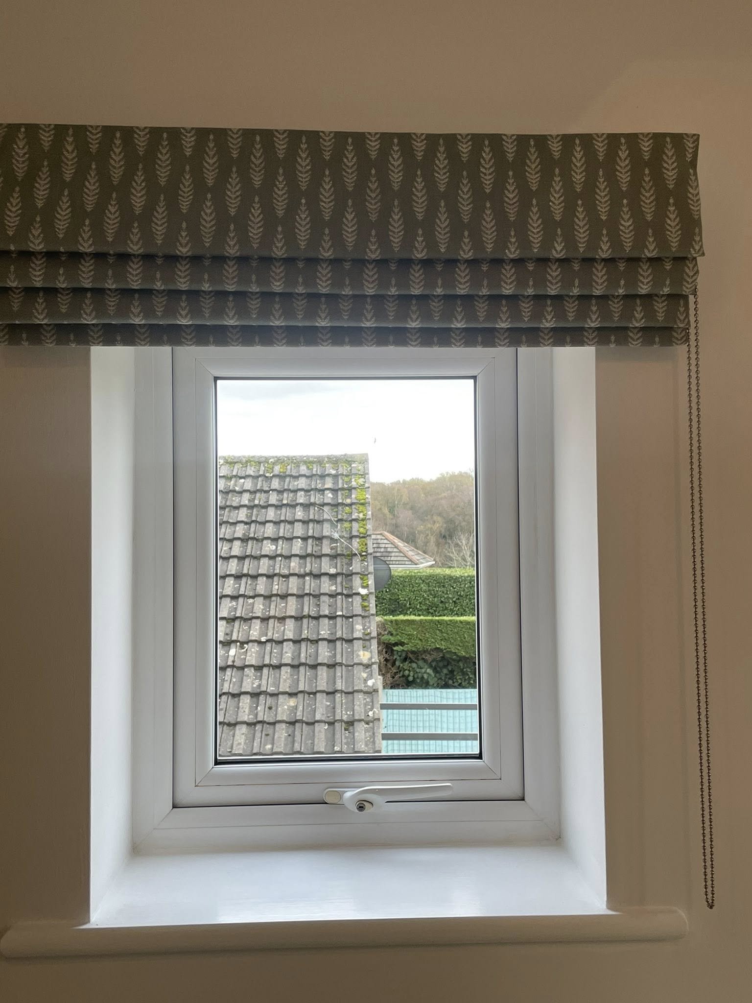 A view through a window showing a tiled roof, trees, and a blue swimming pool in the distance.