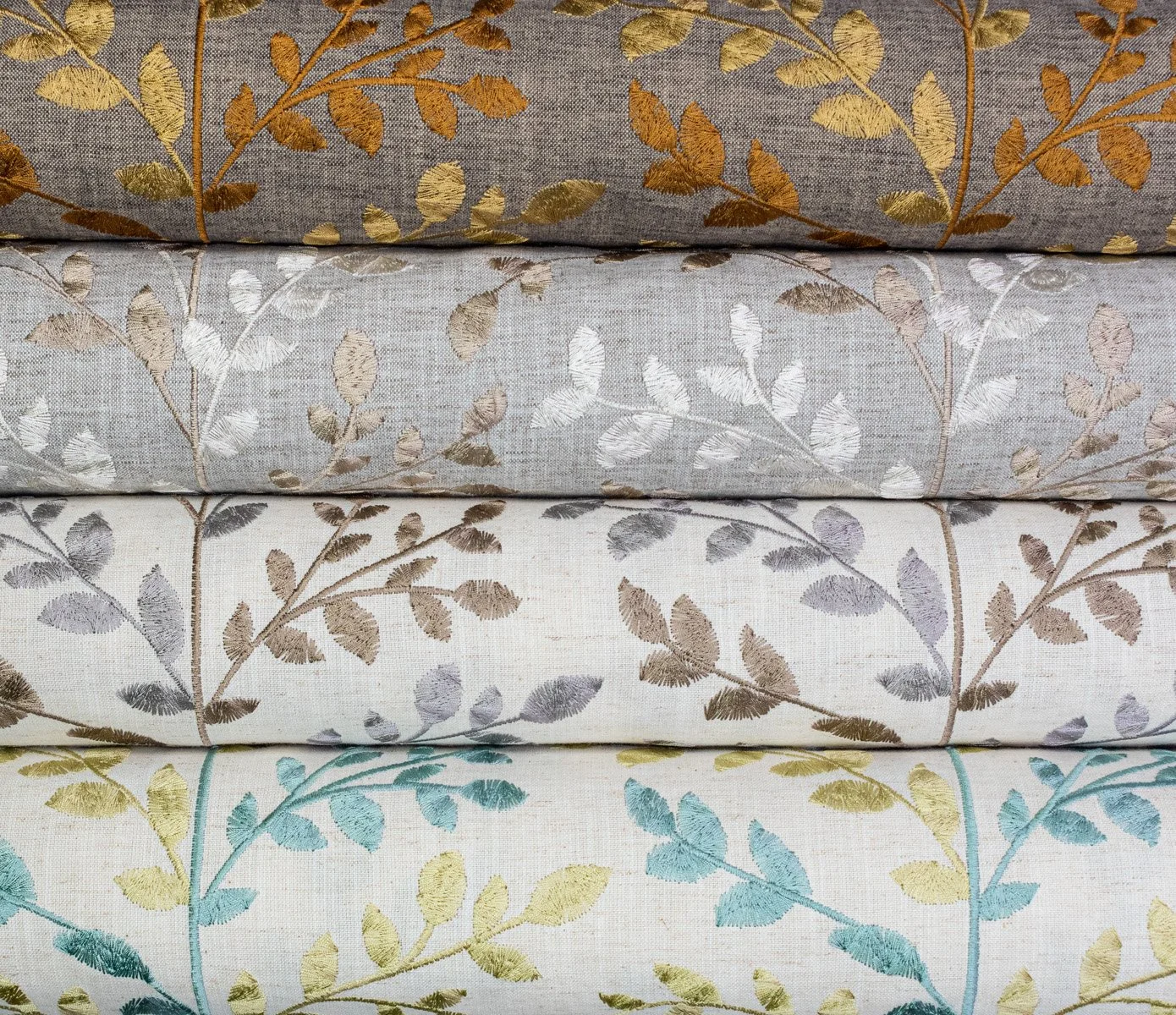Stacked folded curtains with embroidered leaf patterns in various pastel shades, including gray, white, and beige.