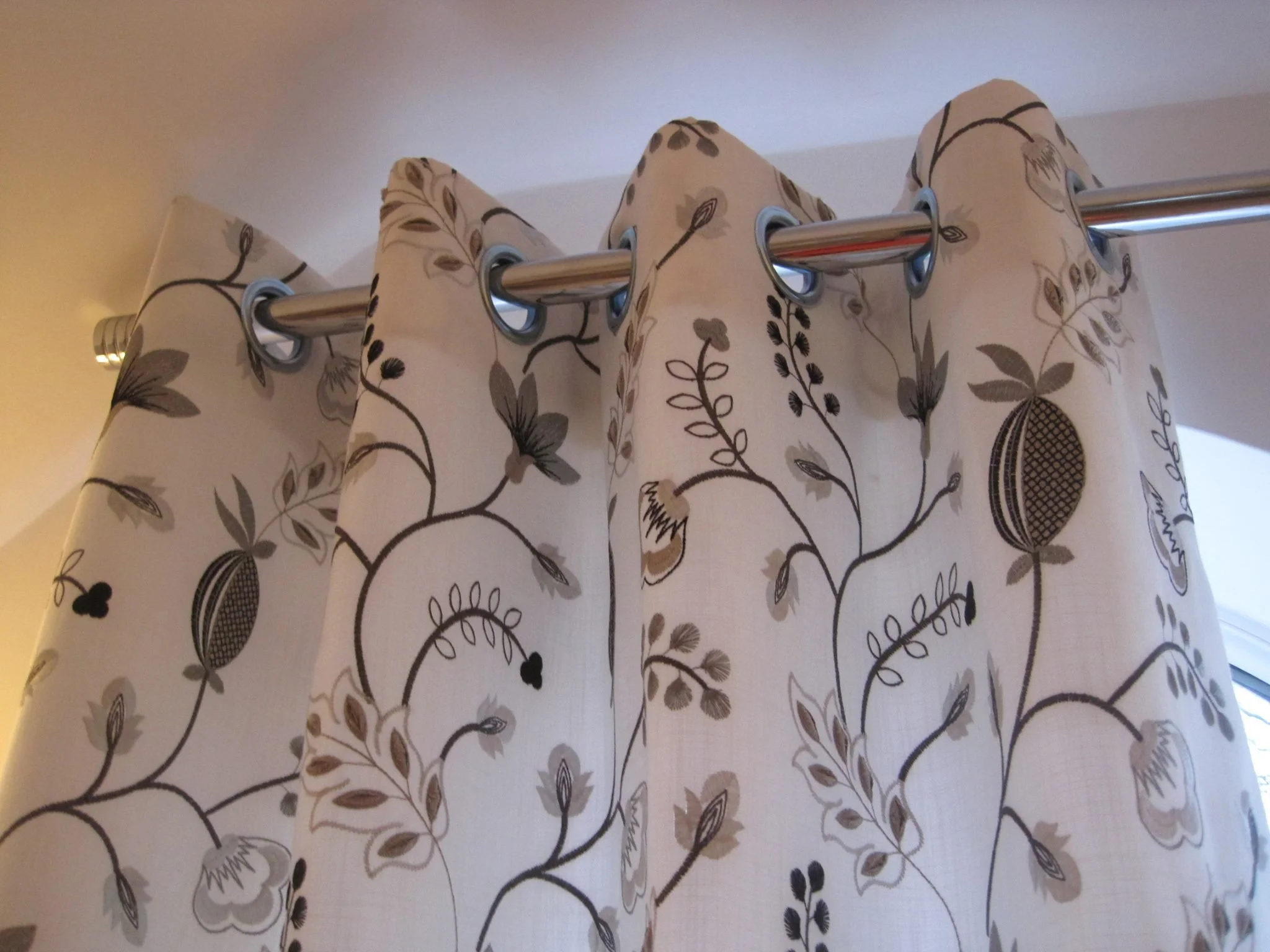 Close-up of a beige curtain with a floral pattern, hanging on a metal rod in front of a window.