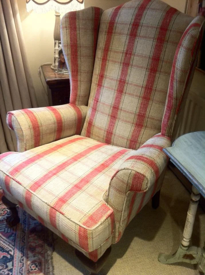 A vintage wingback chair with red and beige plaid upholstery beside an end table with some items on it.