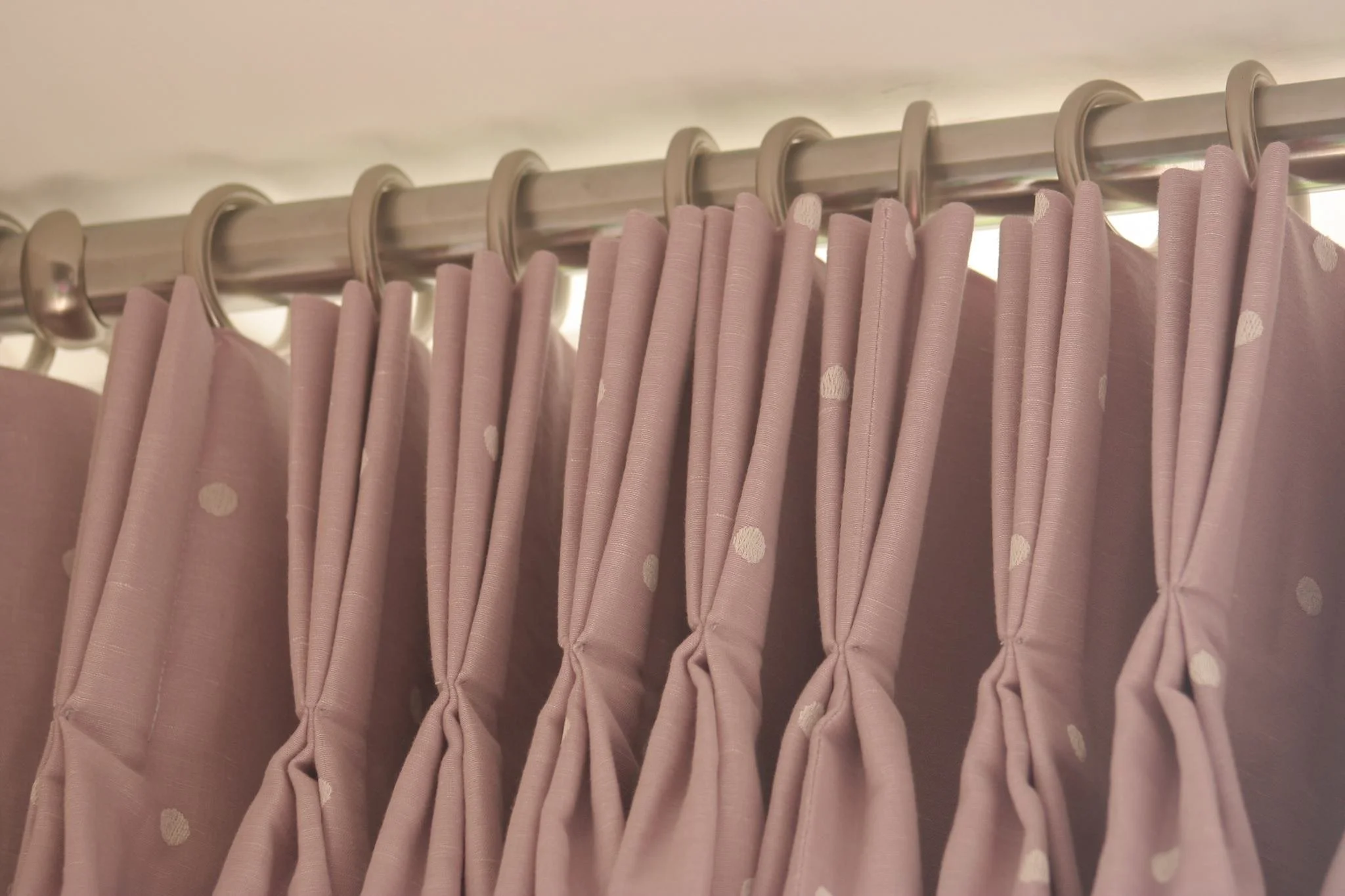 Pink curtain with polka dots hanging from metal curtain rings on a curtain rod.