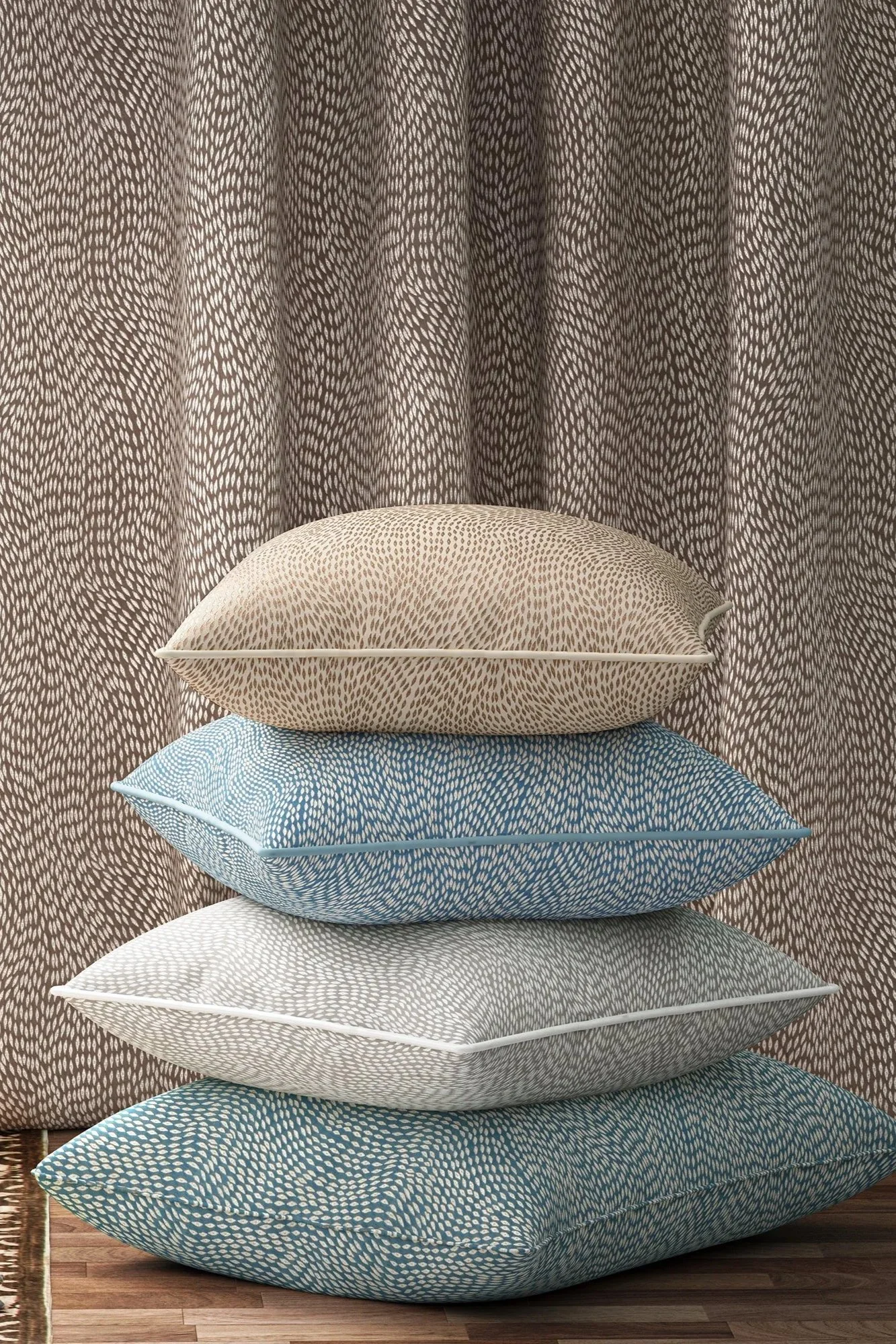 A stack of five cushions with geometric patterns placed on a wooden floor in front of a curtain with a matching geometric pattern.