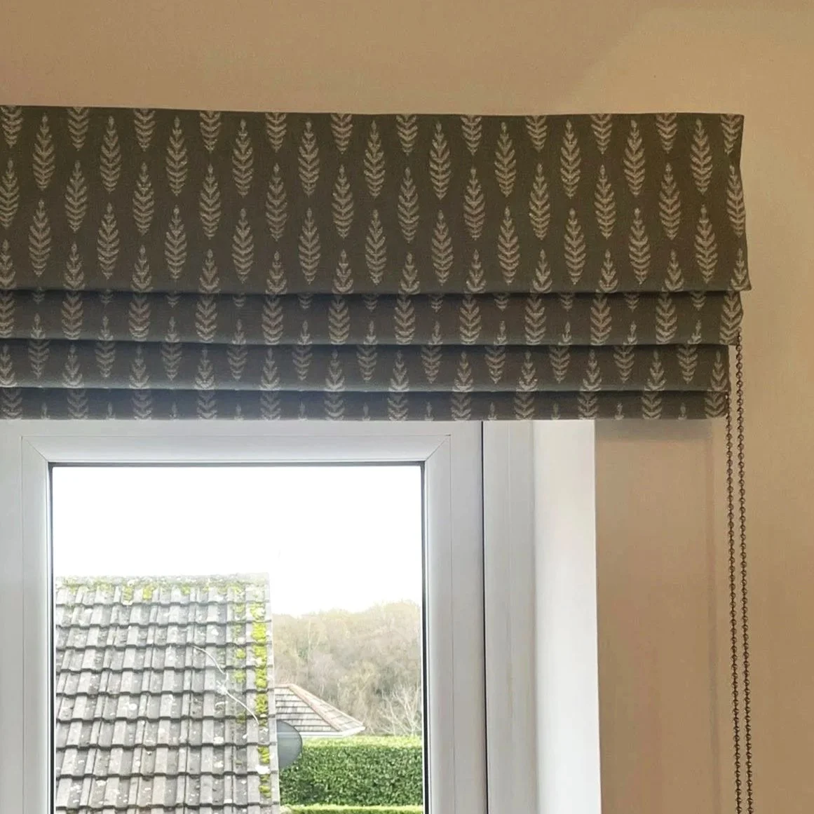 Window with a patterned valance curtain, overlooking a rooftop and trees outside.