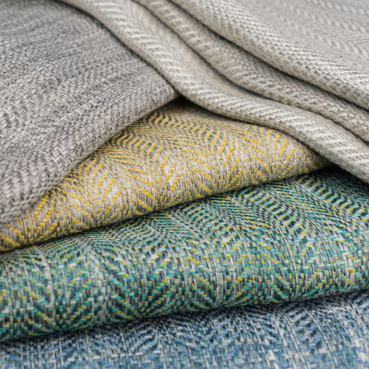 Stacked folded fabric pieces with various patterns and textures in shades of gray, yellow, and teal.