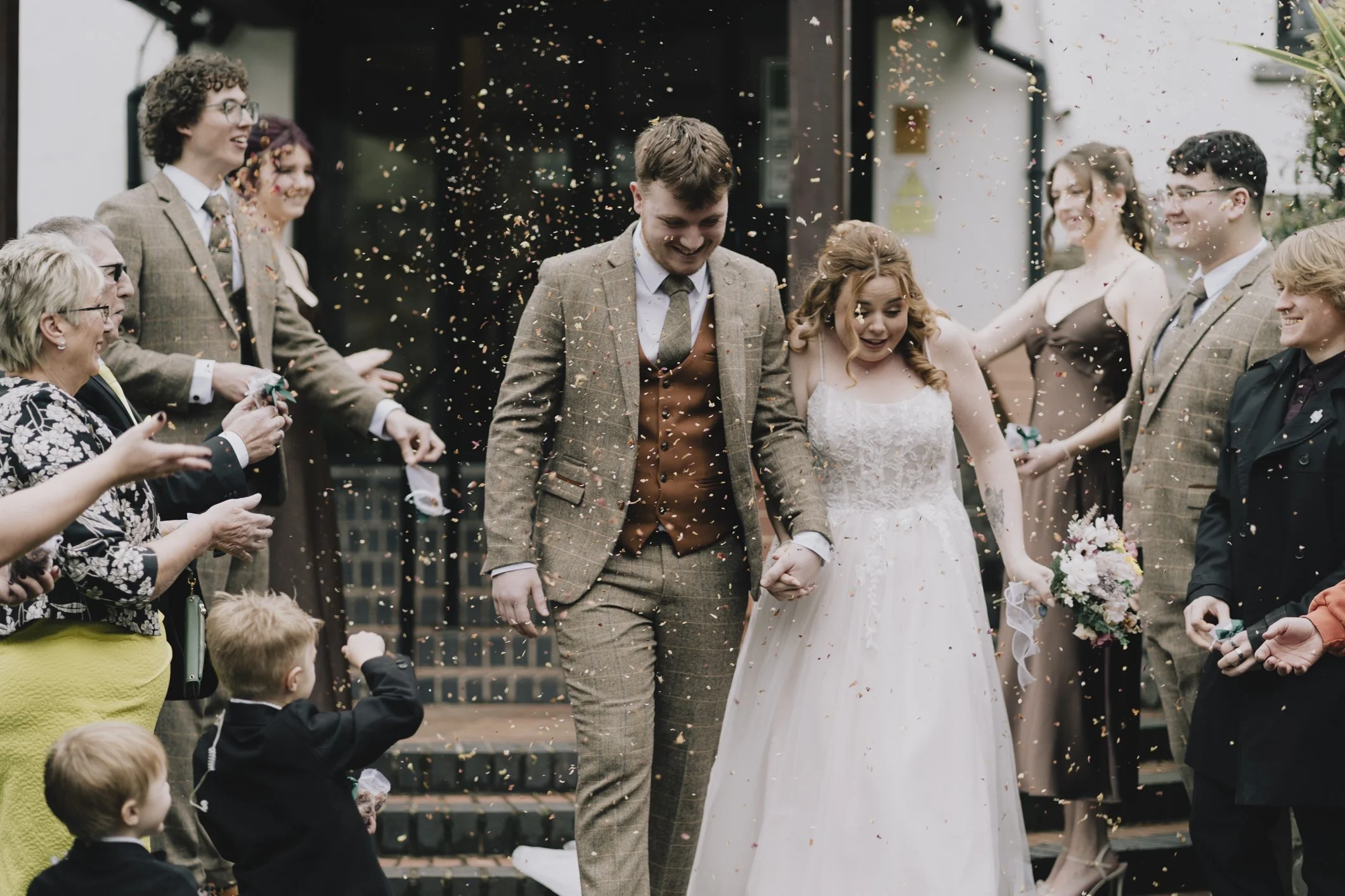 Bride and groom walking hand in hand while guests celebrate with confetti outside Webbington Hotel and Spa