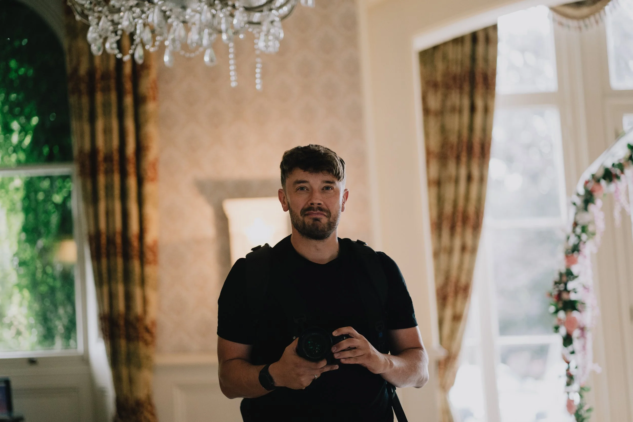 Mike Greenhill Photography taking a photo in a well-lit room with large windows, floral curtains, and a chandelier. Mike is a Bristol Wedding Photographer