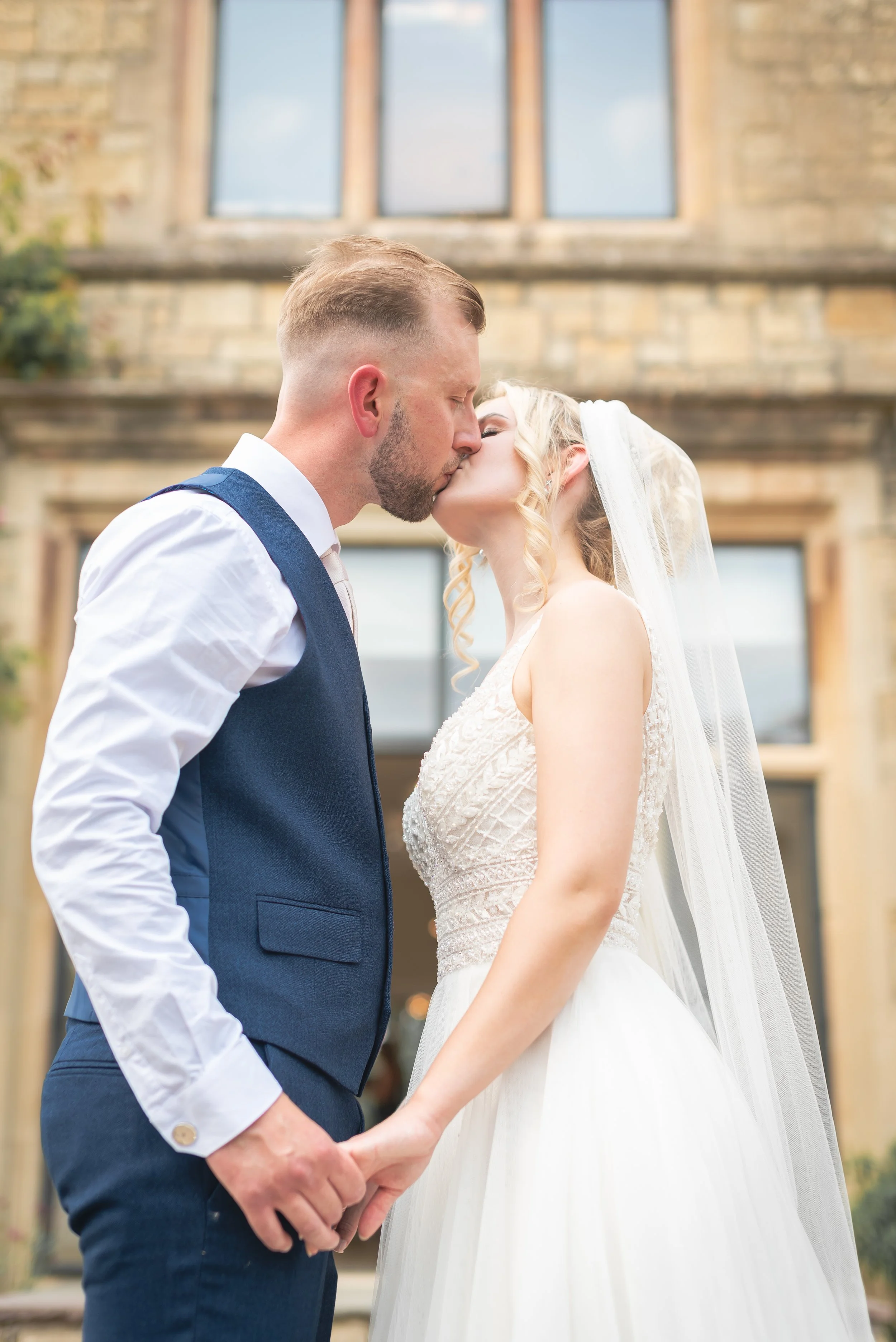 A bride and groom sharing a kiss outdoors in front of Old Down Estate captured by Bristol Wedding Photographer