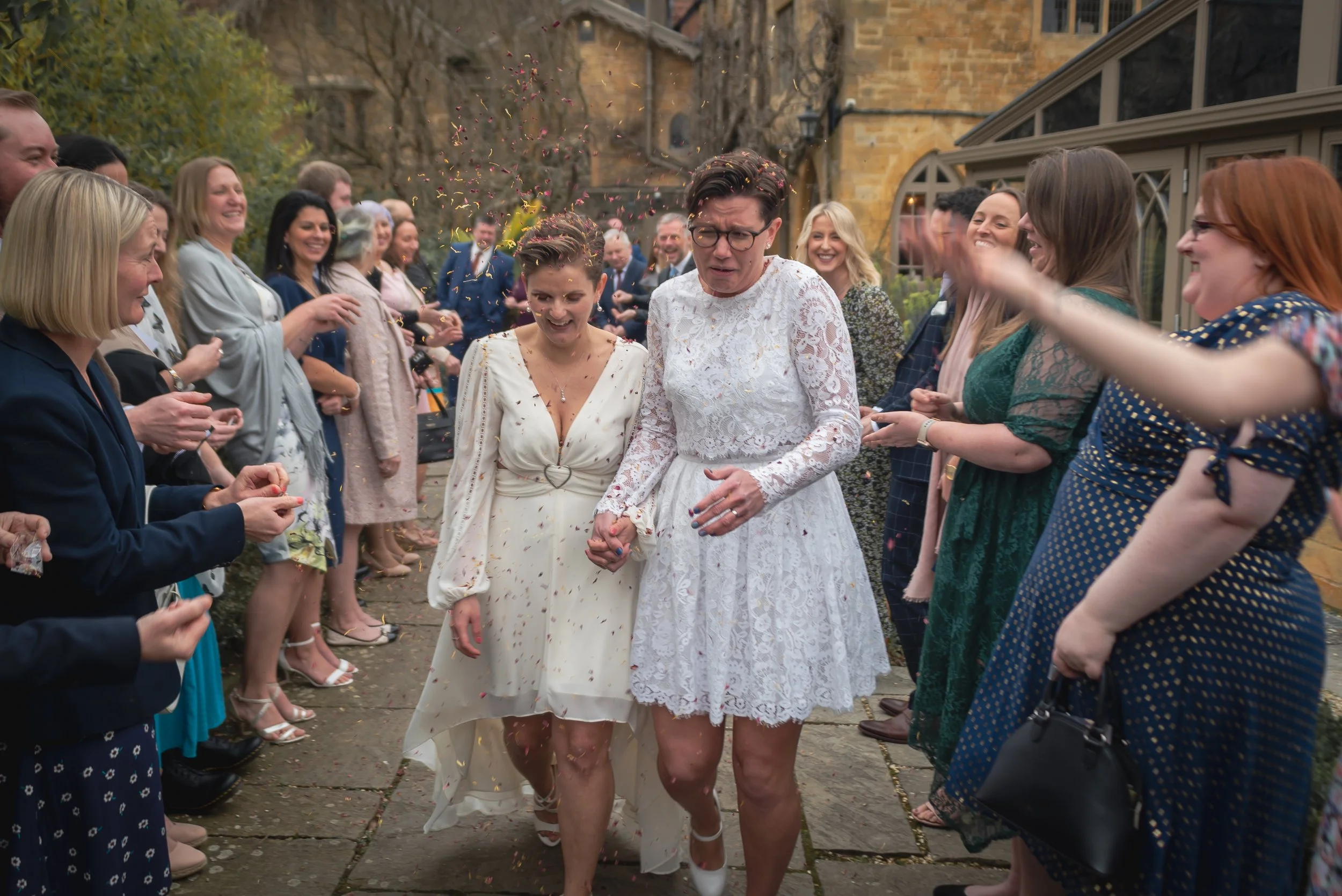 People celebrating wedding with confetti in an outdoor garden courtyard with historic Manor House, Moreto-in-Marsh in the background.