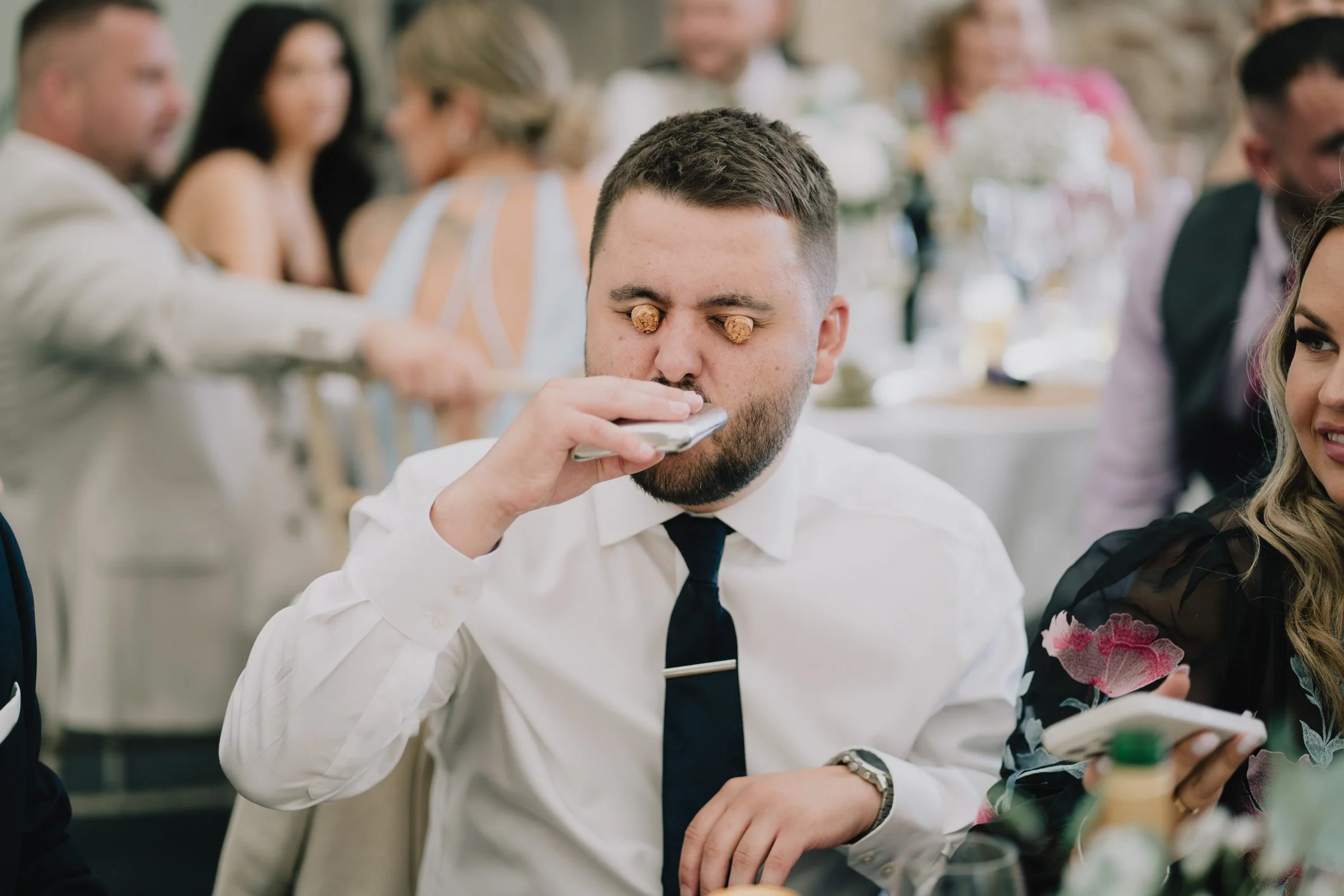 Guest drinking from hip flask with corks in his eyes taken by documentary wedding photographer in Bristol