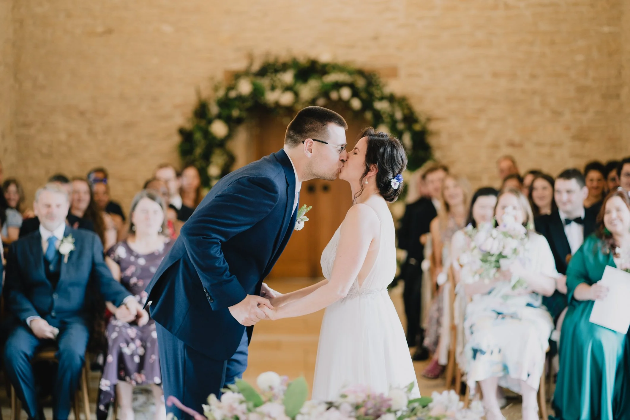 Bride and groom sharing their first kiss as a married couple during the ceremony at Kingscote Barn