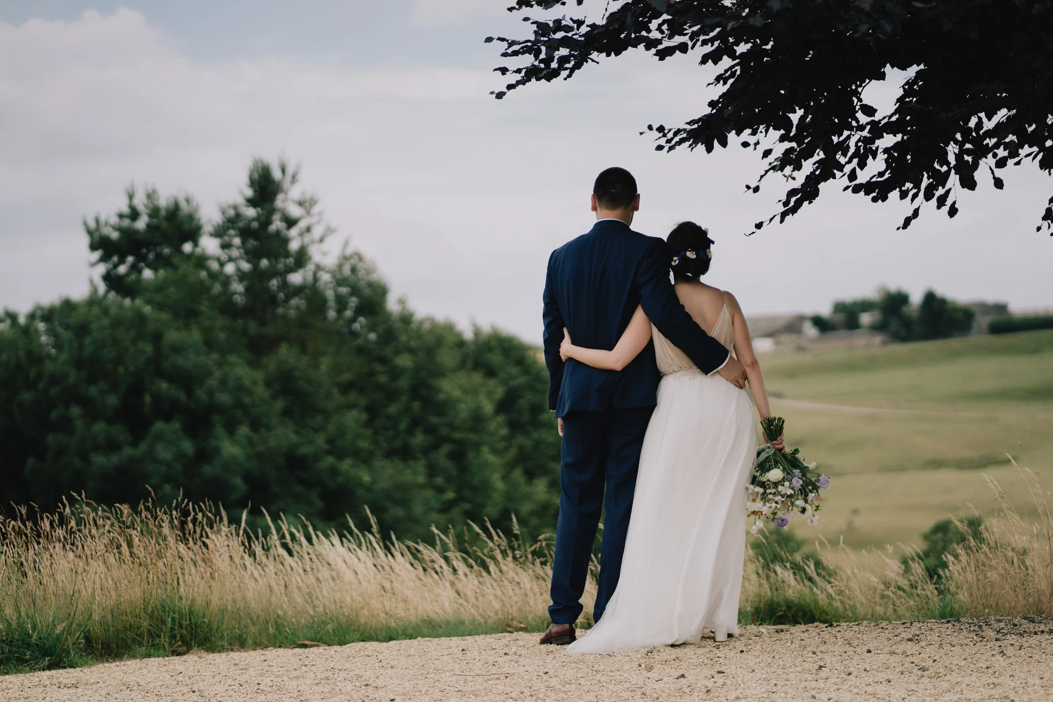 Bride and groom holding each other and looking out over the Cotswolds countryside