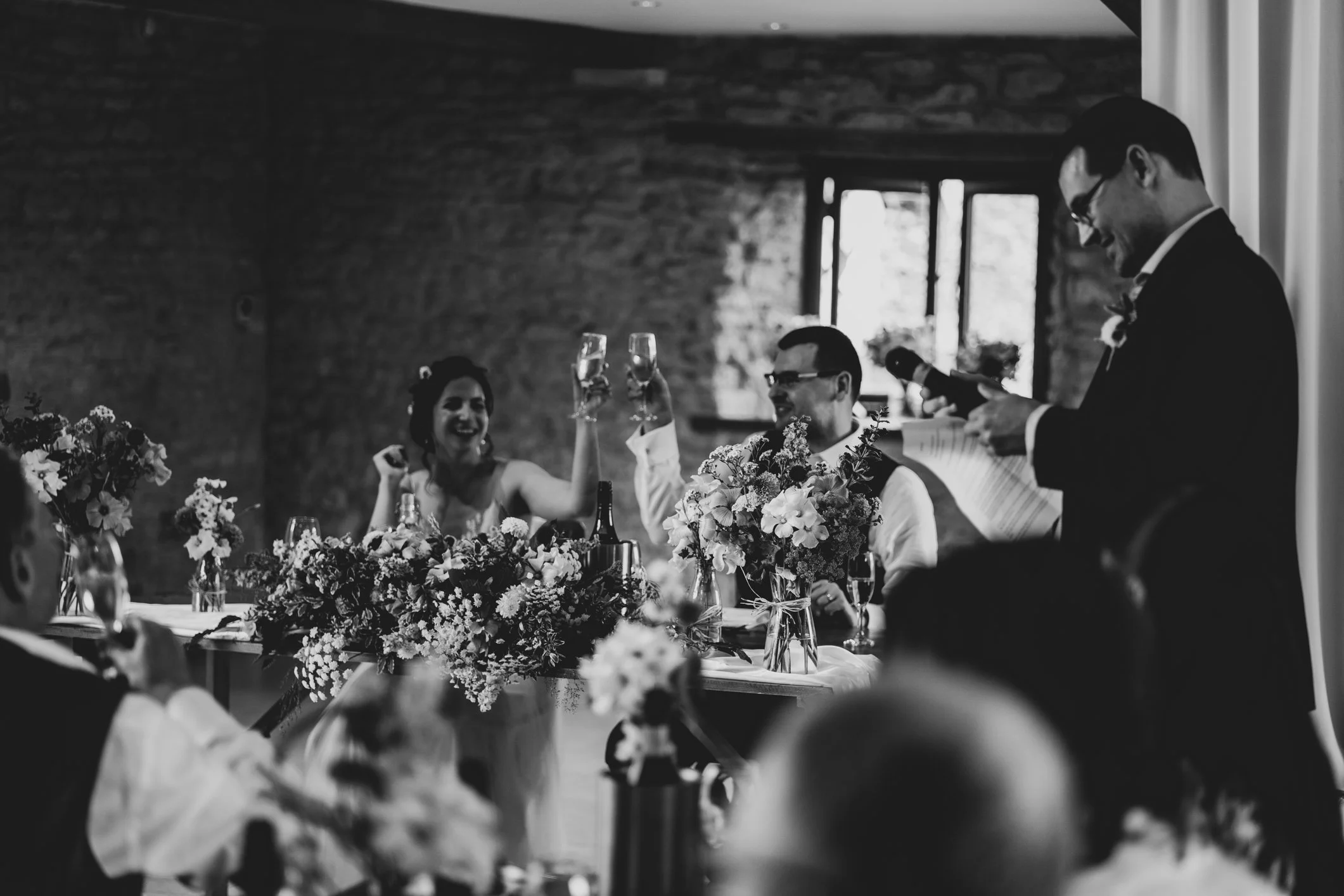 Couple raising glasses in celebration during the best man’s wedding speech