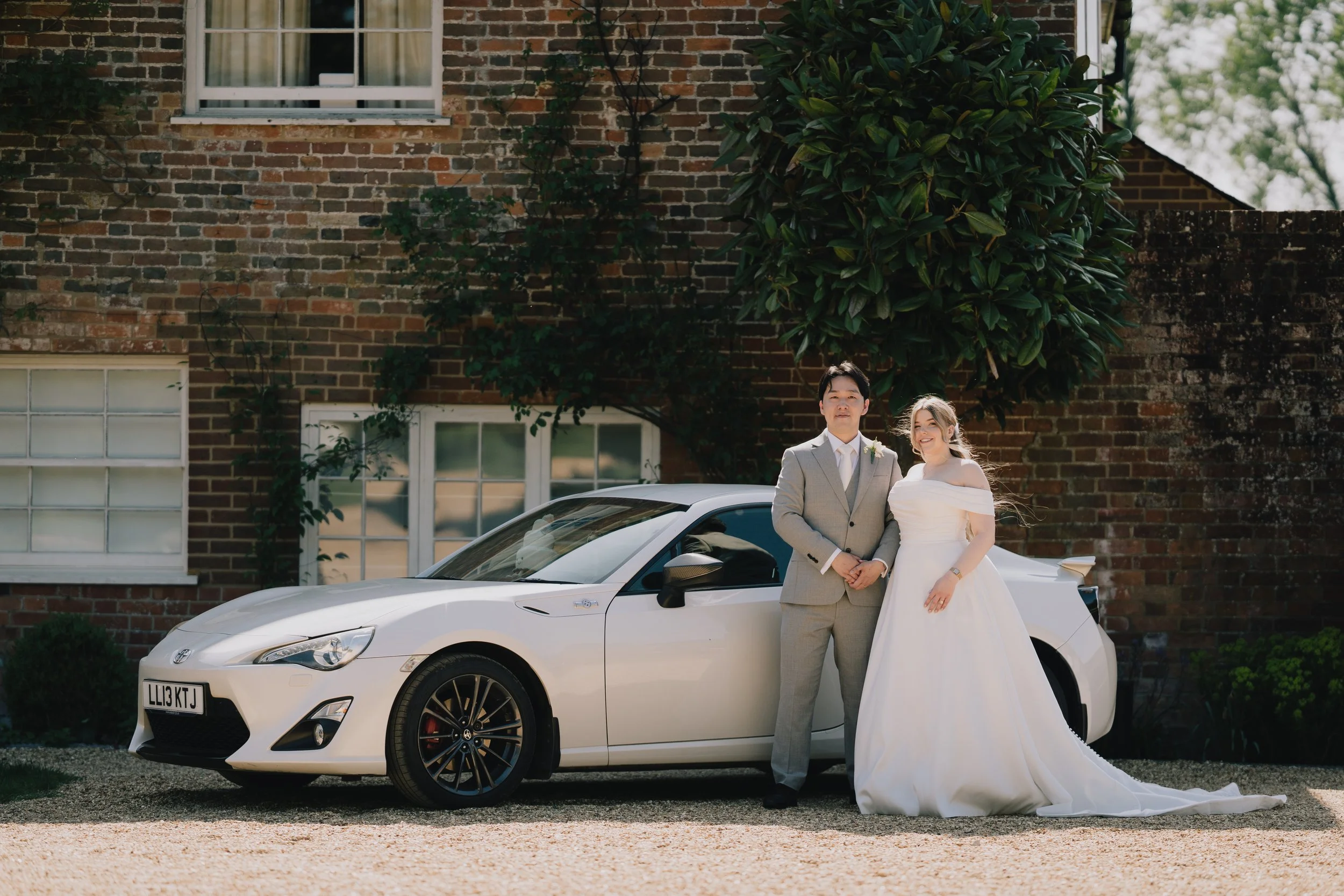 Bride and groom standing next to classic wedding car outside Syrencot country house