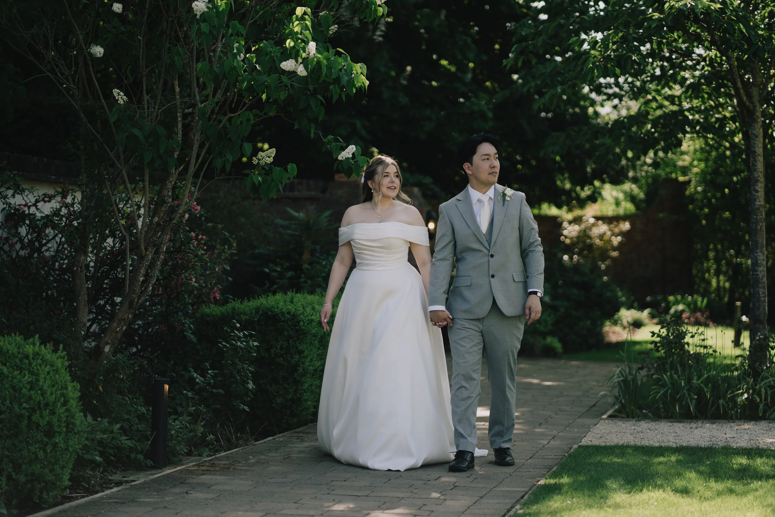 Romantic moment of Lucy and Kevin walking hand-in-hand down garden path at Syrencot