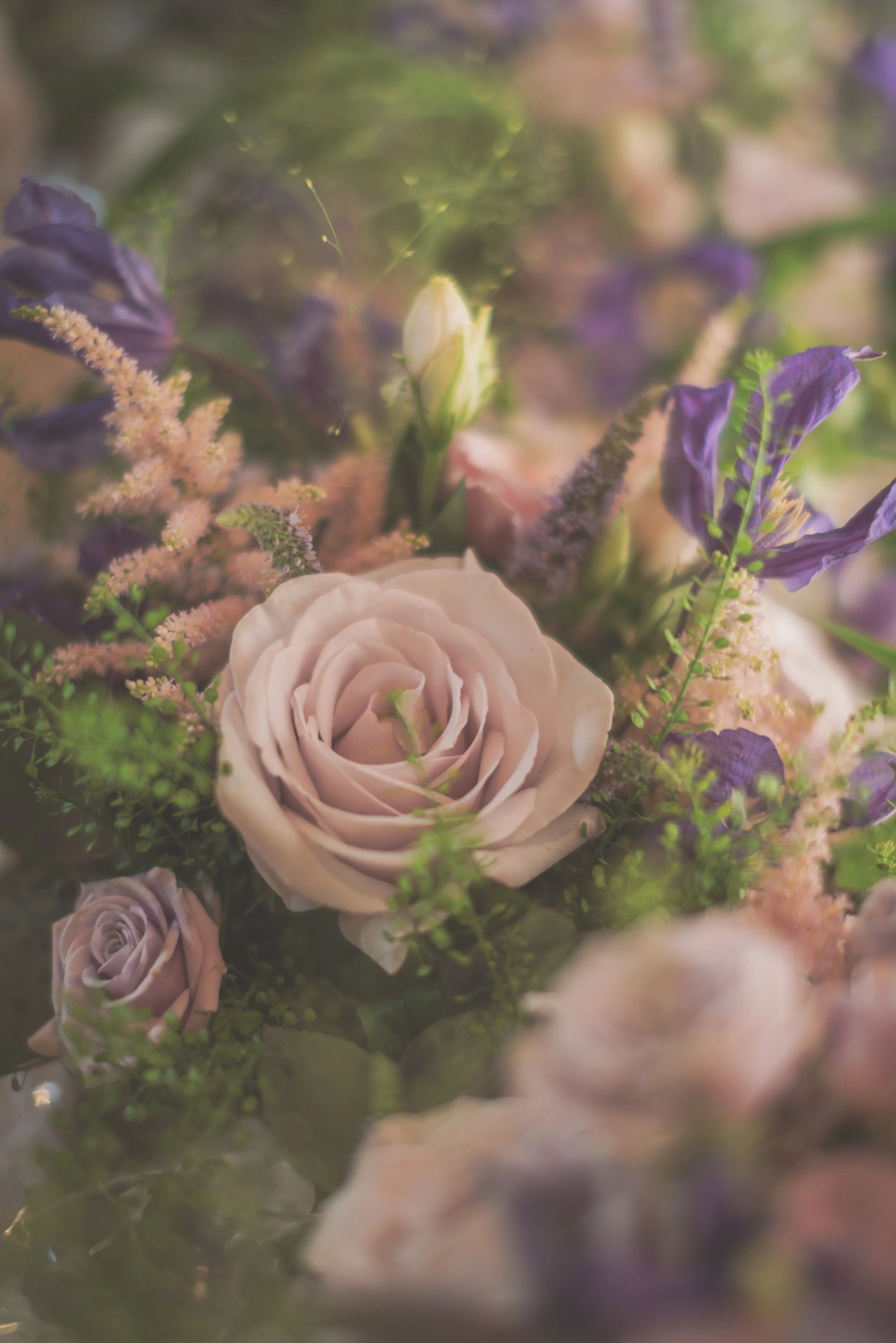 A close-up of a floral arrangement with pale pink roses, purple flowers, and greenery.