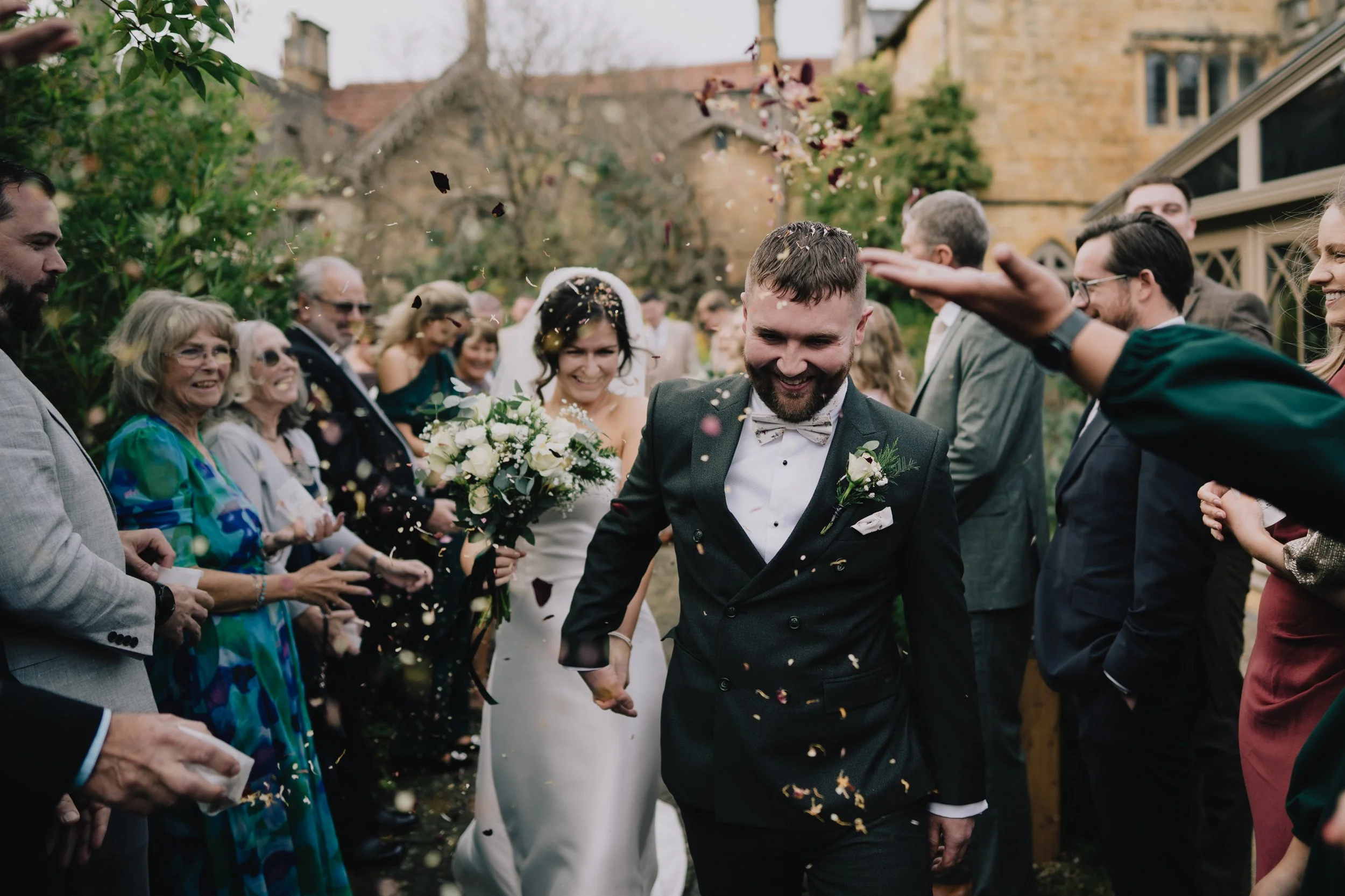 Wedding celebration with the bride and groom walking through a shower of confetti, surrounded by guests outside in a garden or yard at a Bristol wedding