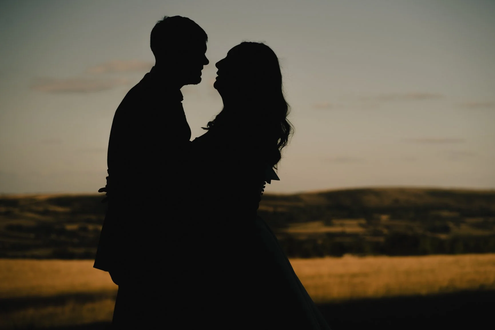 Silhouette of a man and woman facing each other closely against a sunset background.