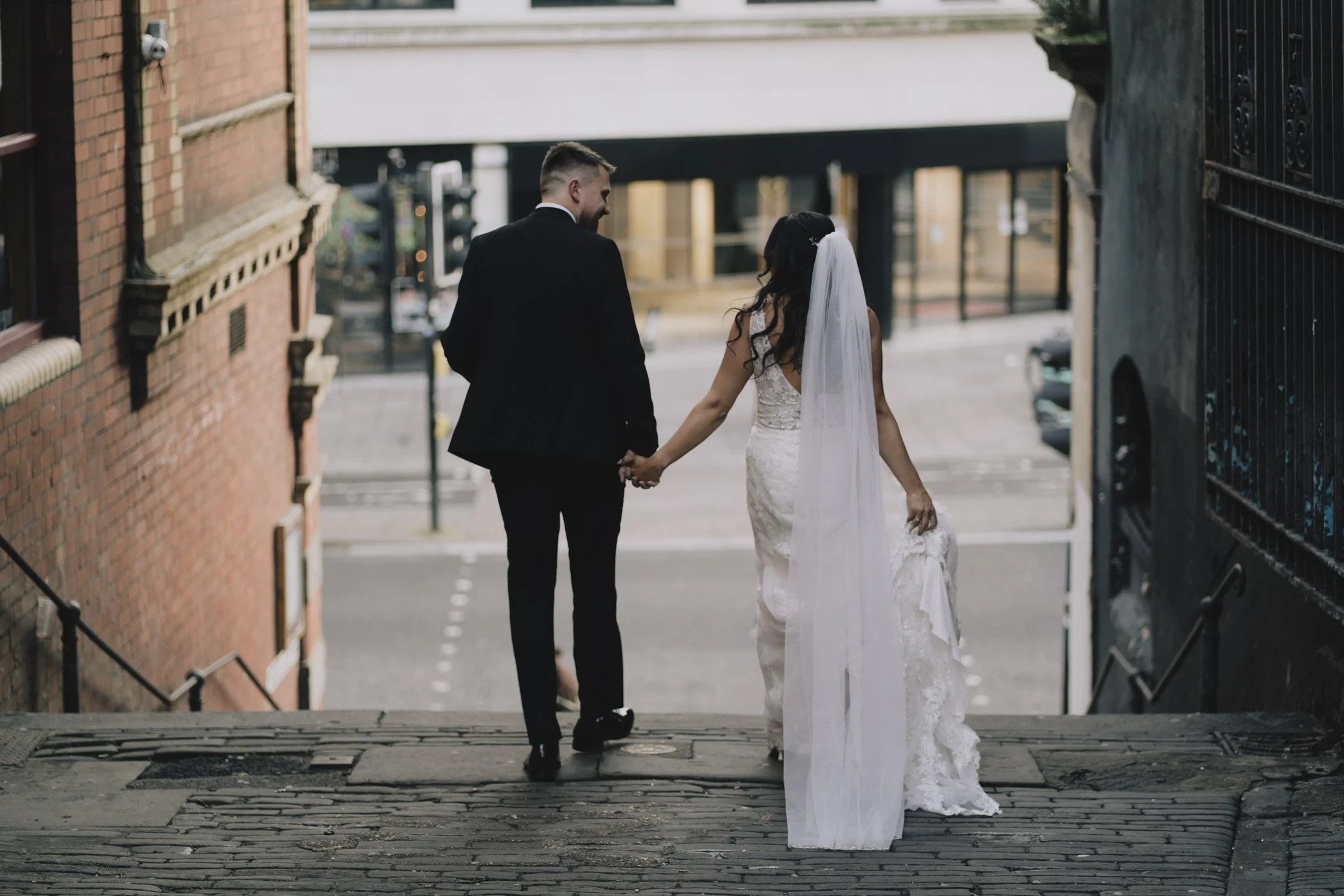 A newlywed couple holding hands walking down a city street stairway in Bristol in wedding attire.