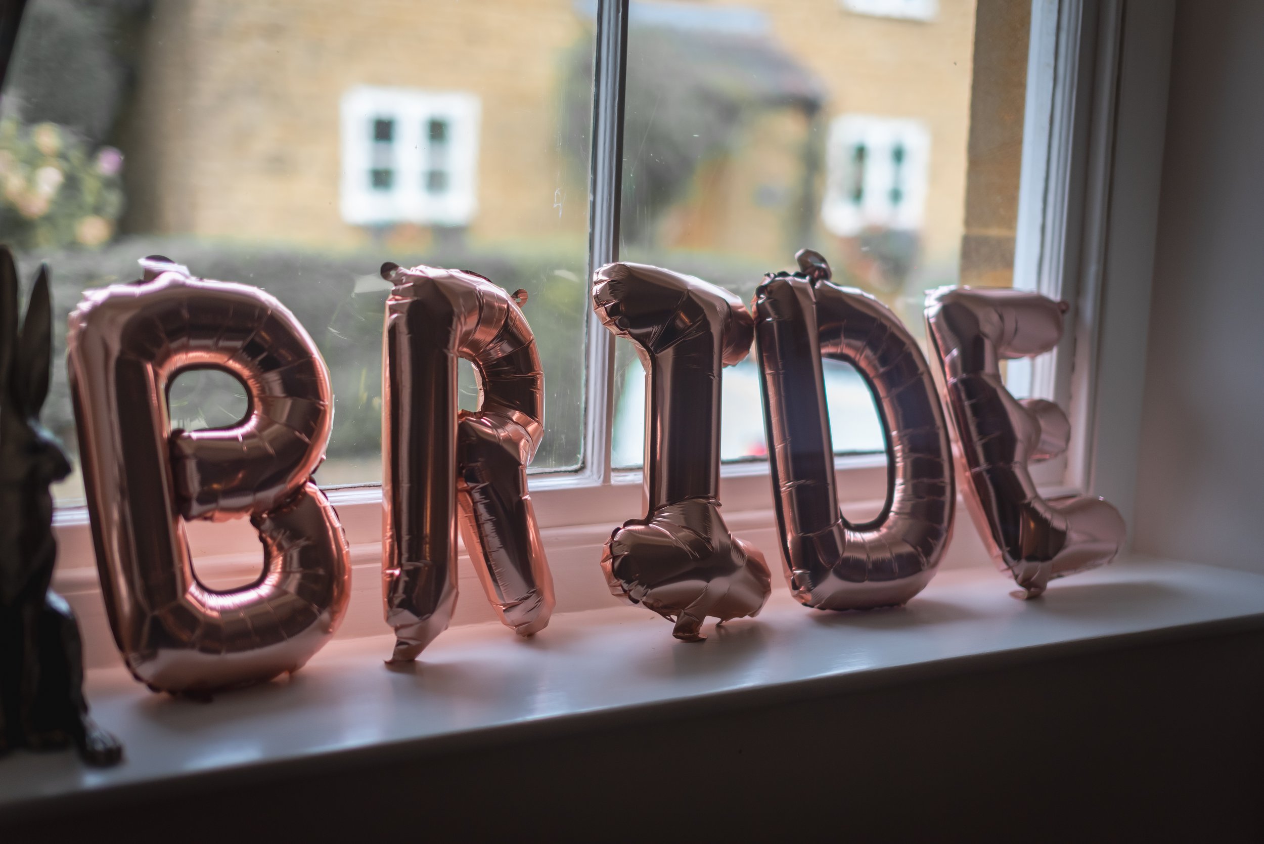 Rose gold foil letter balloons spelling 'BRIDE' on a window sill during morning prep photography in Somerset