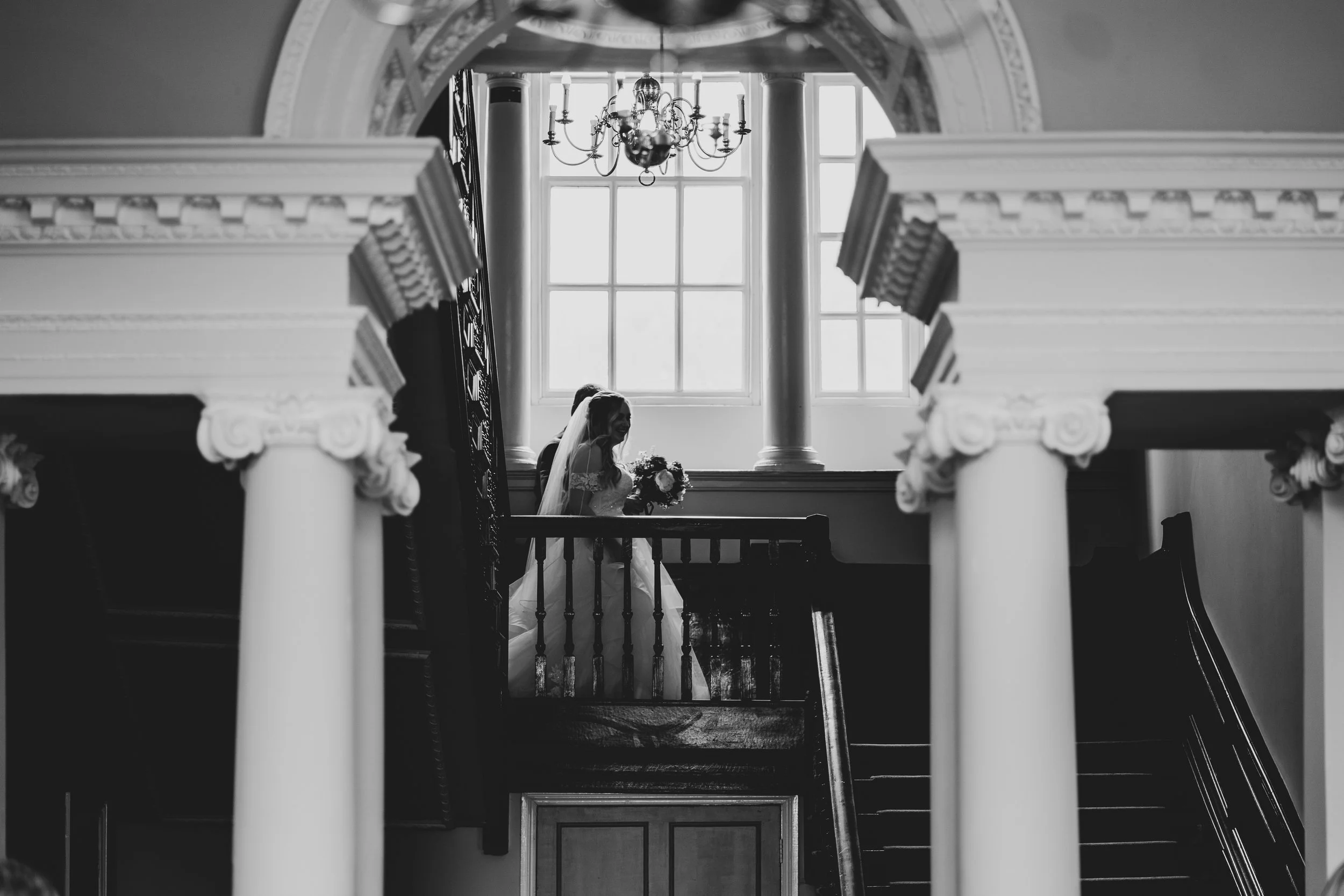 Black and white photo of bride walking towards wedding ceremony in front of large Georgian window at Crowcombe Court.