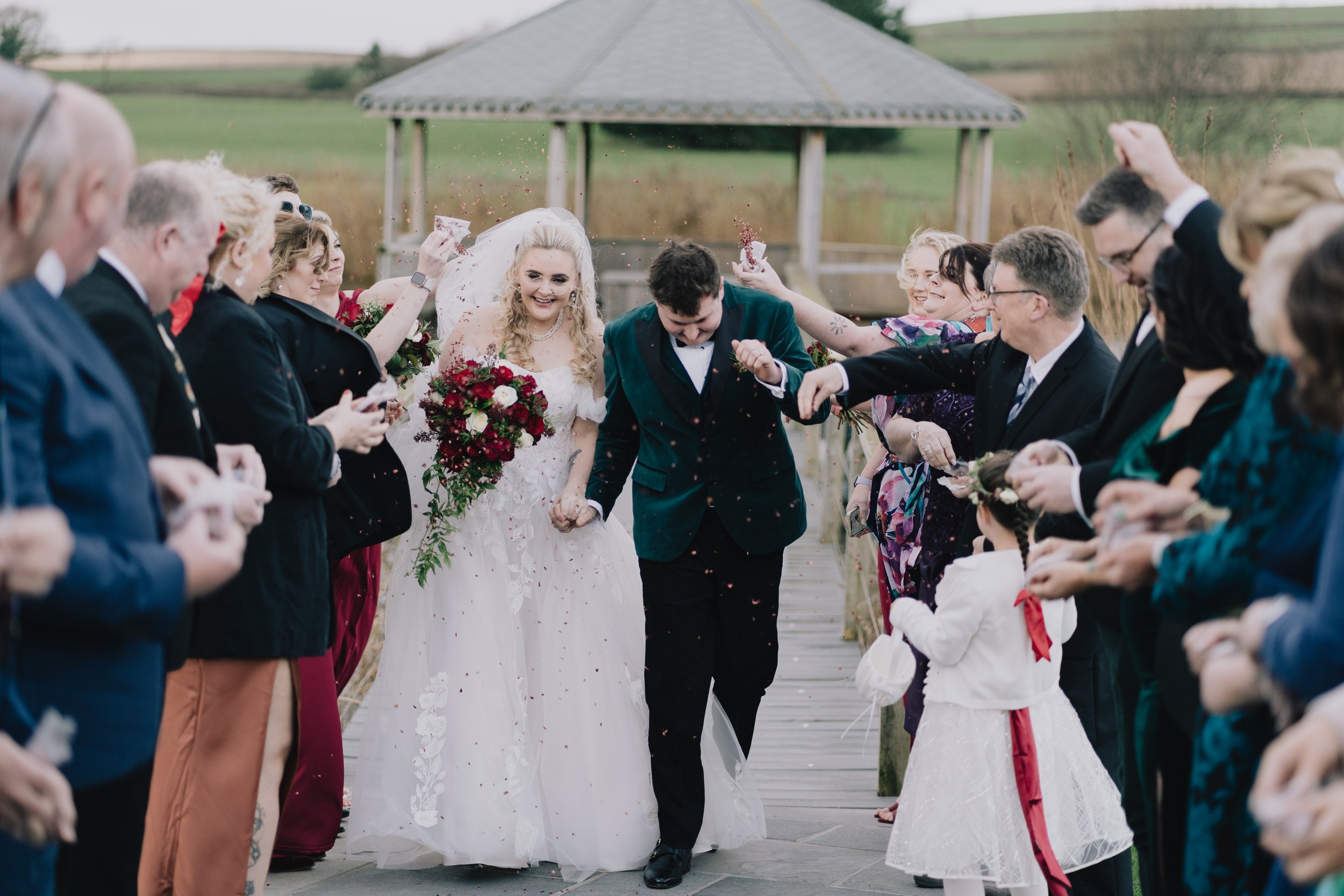 Bride and groom walking through a festive confetti throw outside Quantock Lakes after their winter wedding ceremony.