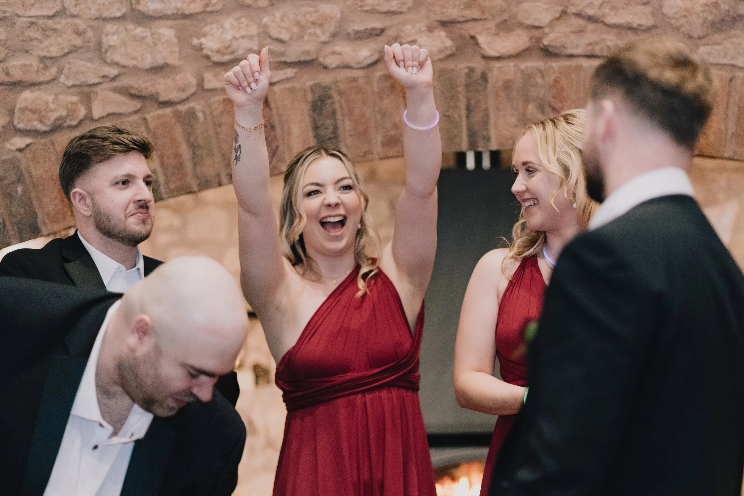 Bridesmaid celebrating with wedding guests, cheering and laughing after doing festive shots during reception at Quantock Lakes.