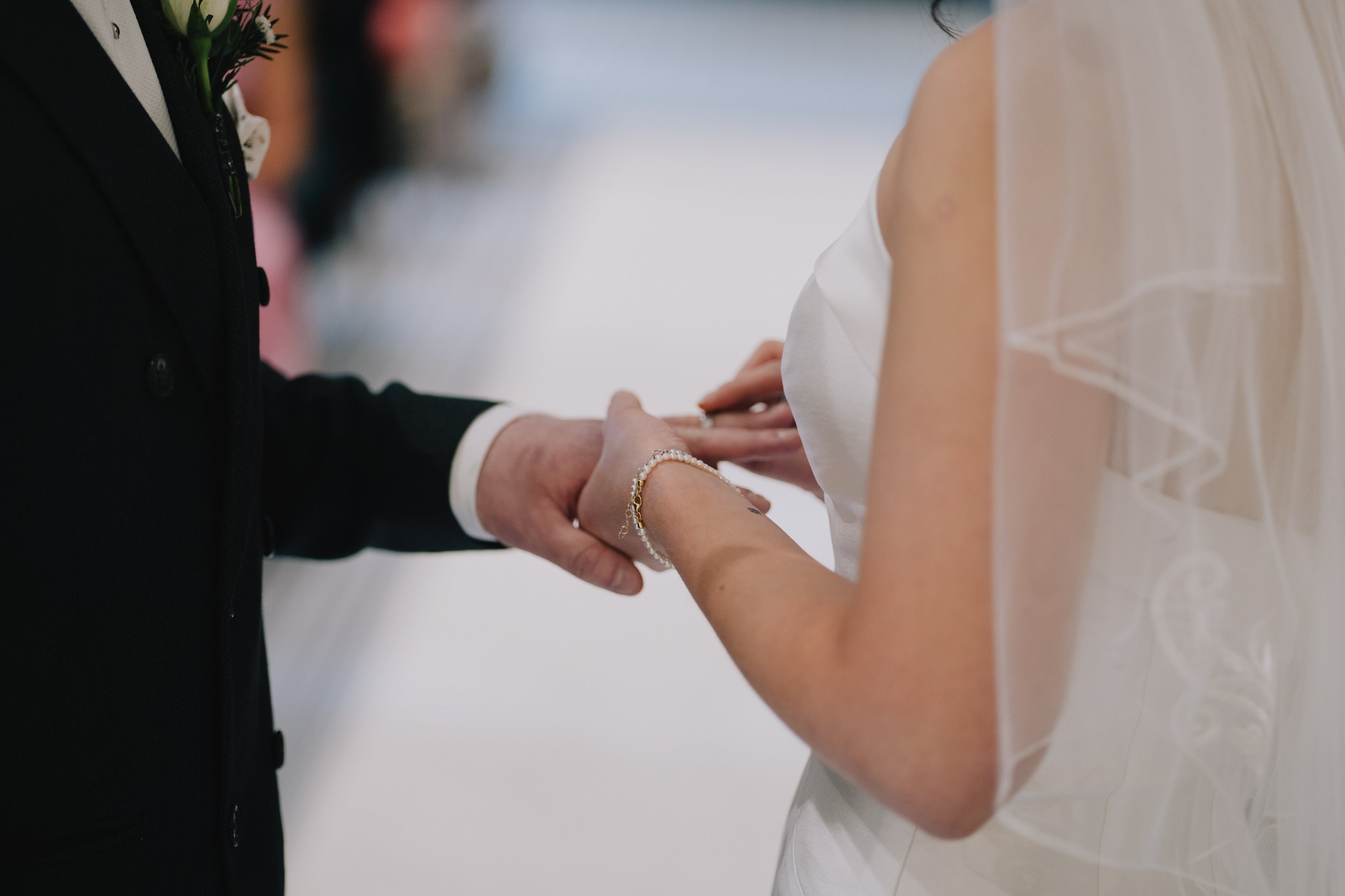 Close-up of a bride and groom holding hands during a wedding ceremony, focusing on their hands and wedding rings in Cotswolds.