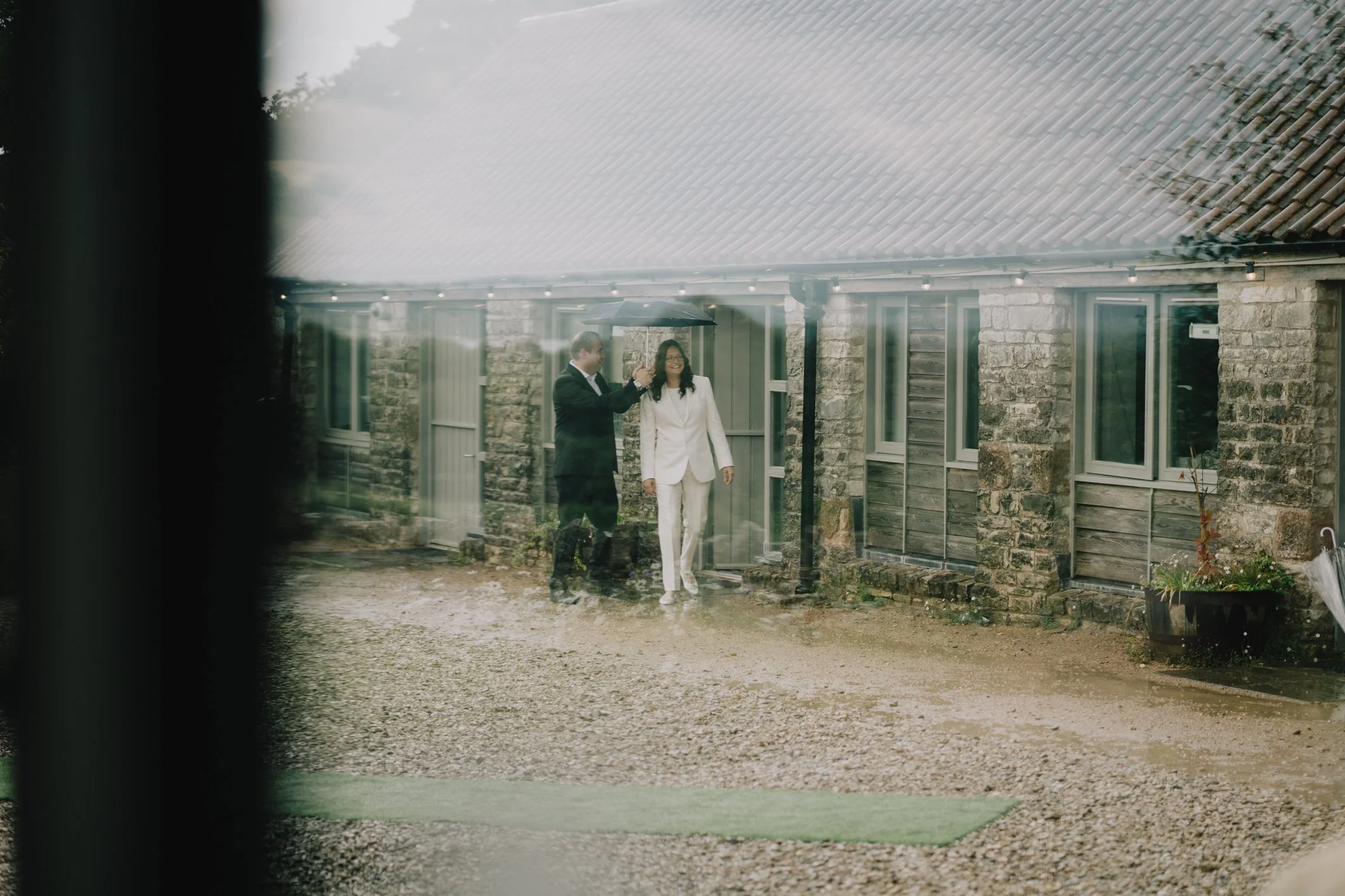 Bride being escorted to ceremony with umbrella due to rain at Folly Farm