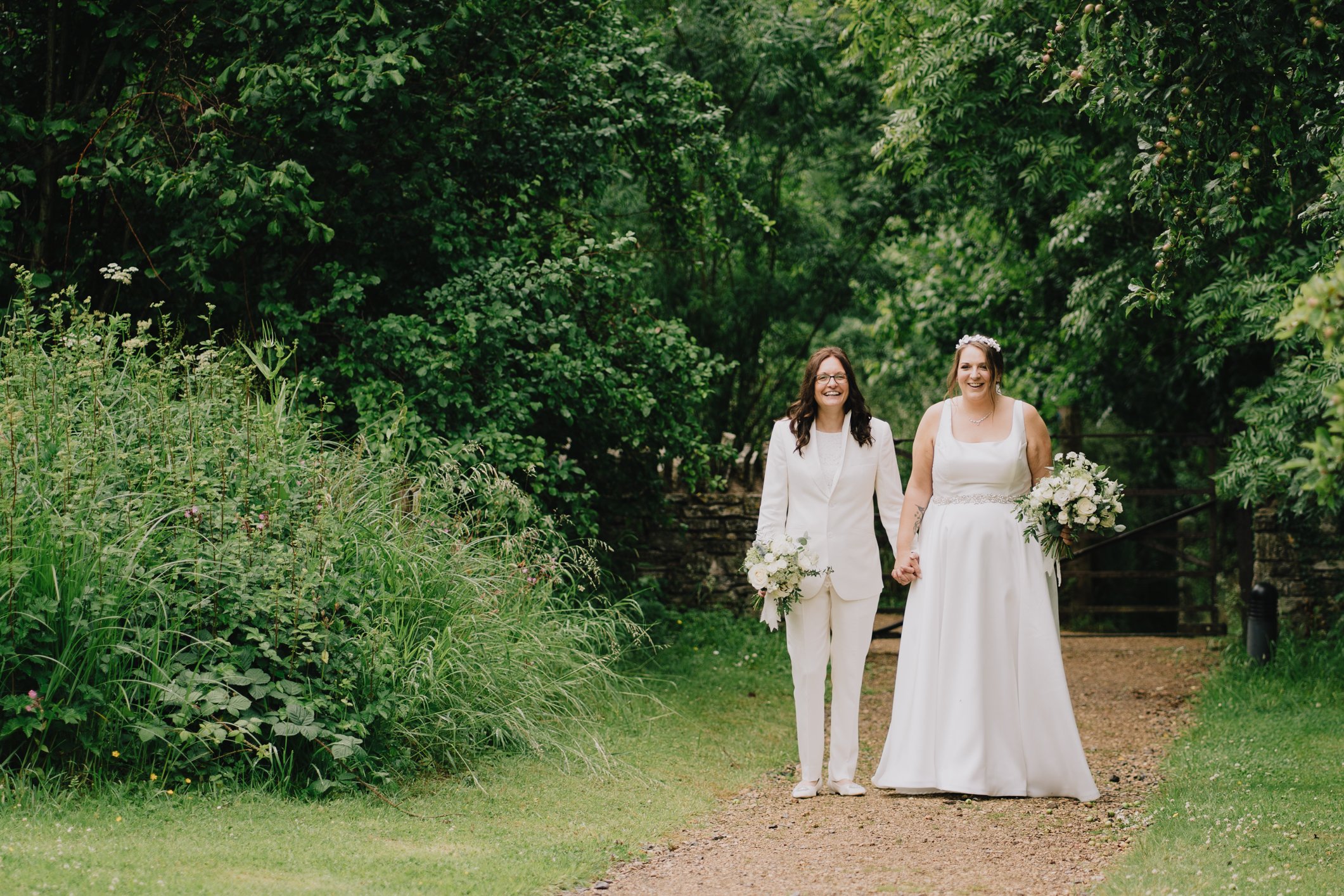 Brides walking up path at Folly Farm Somerset hand in hand