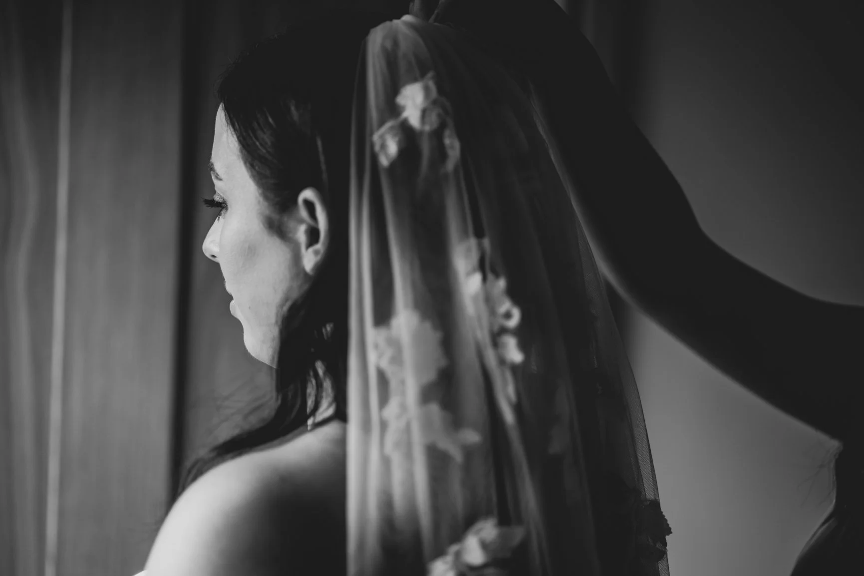 A black-and-white close-up side profile of a bride with a veil on her head, standing by a wall at Oxleaze Barn.