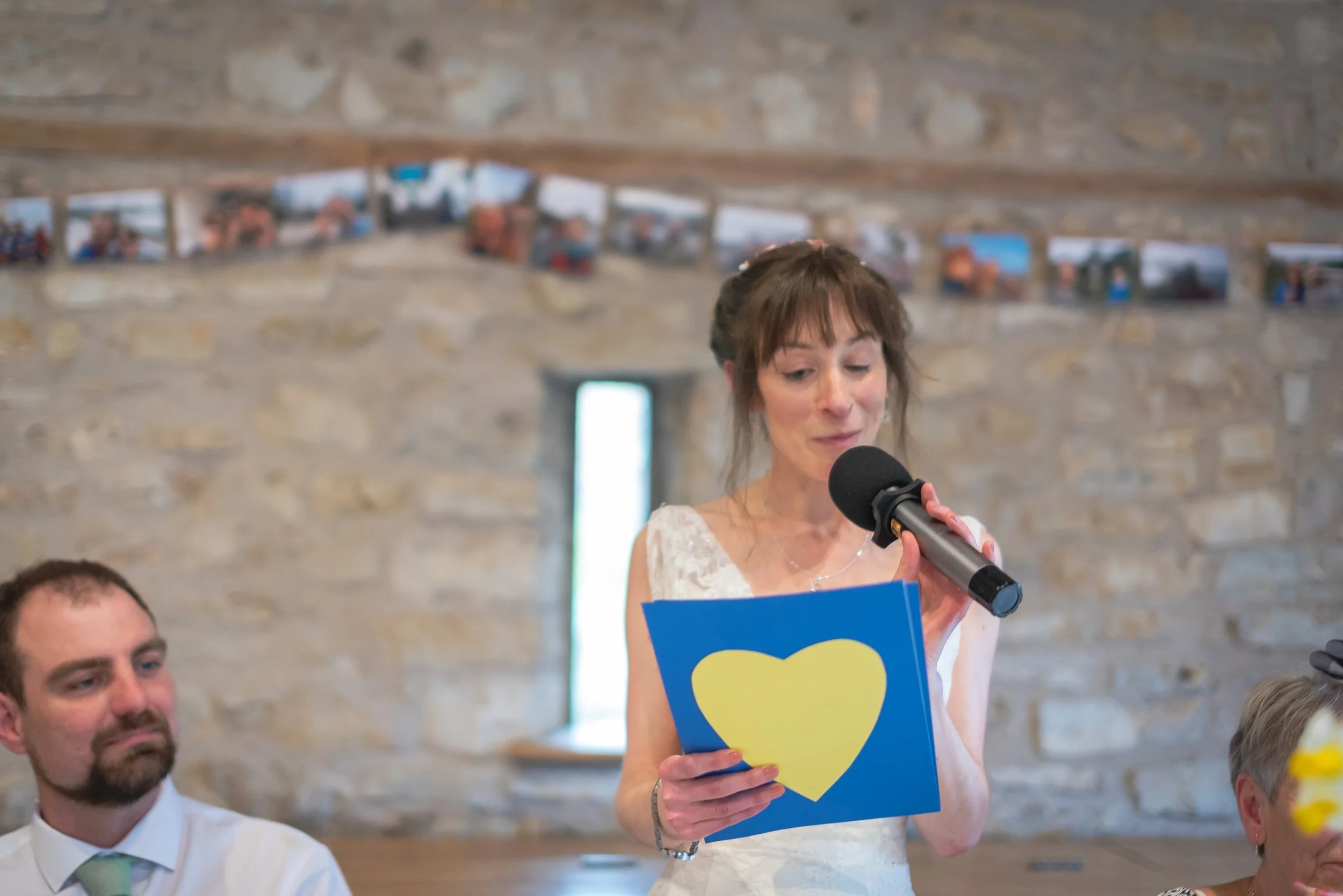 Folly Farm Wedding Photographer captures  bride reading prepared speech with a heart symbol on the paper at a wedding reception.