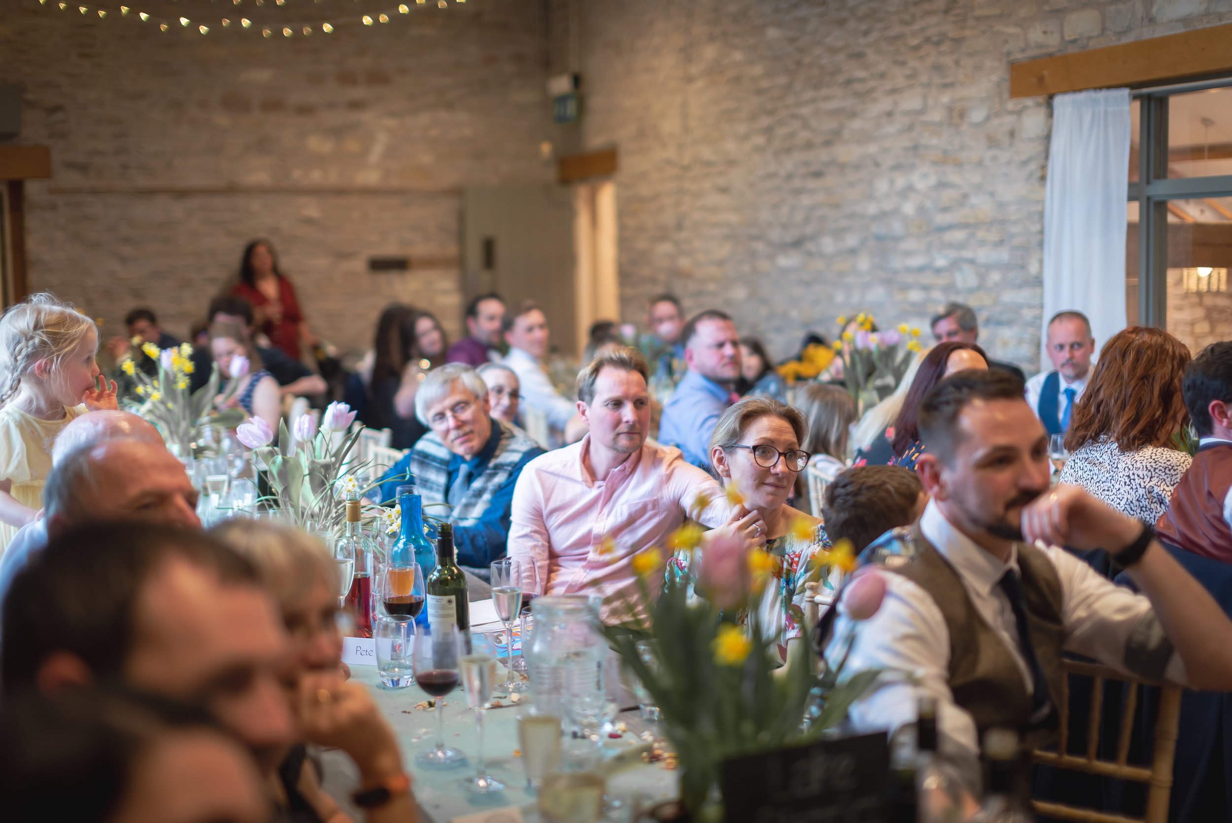 Wedding guests sitting at decorated tables during a social event or celebration inside Folly Farm captured bt Bristol wedding photographer.