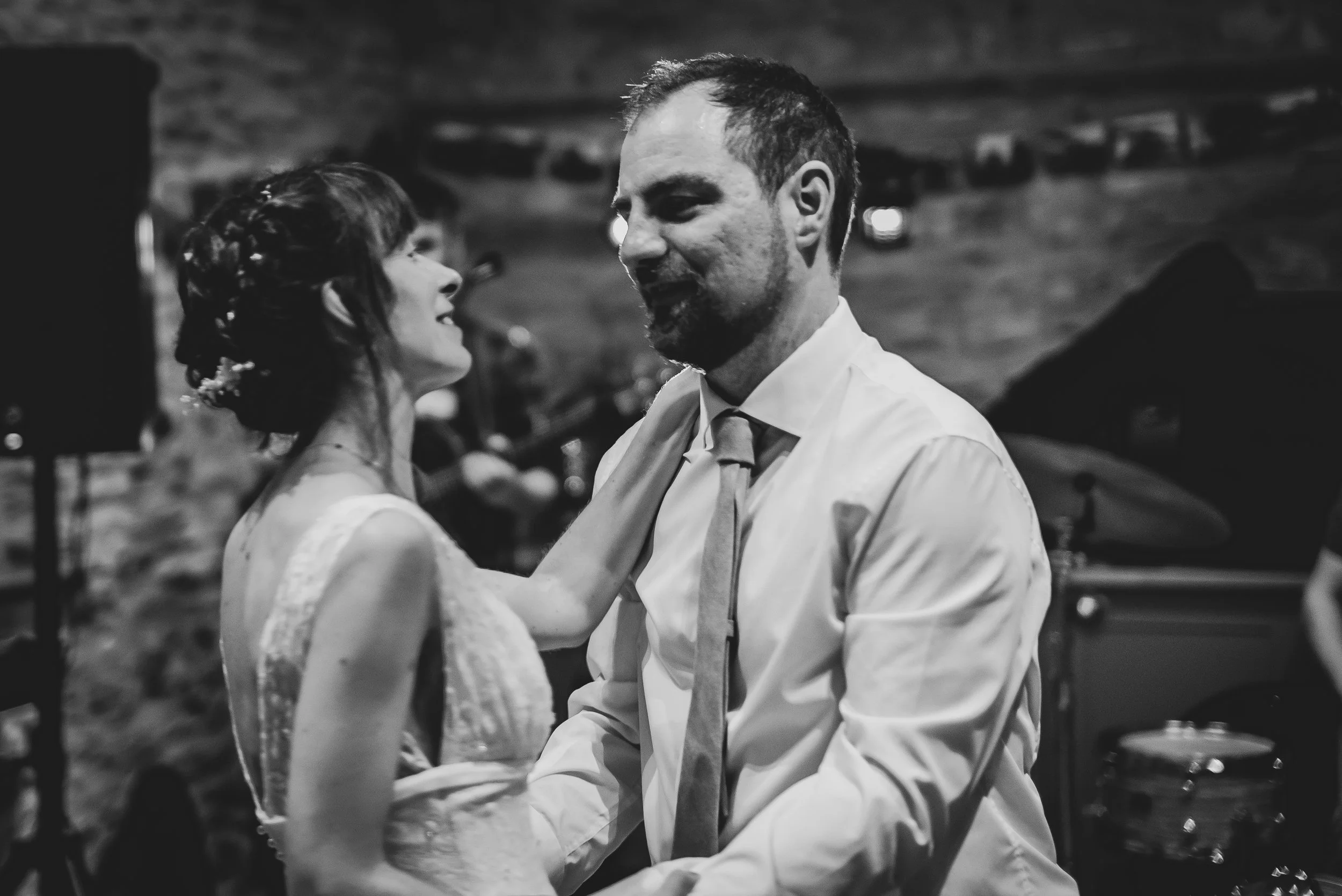 South West wedding photographer captures a bride and groom dancing at their wedding reception, both smiling and looking at each other, with a blurred background of musicians and a piano.