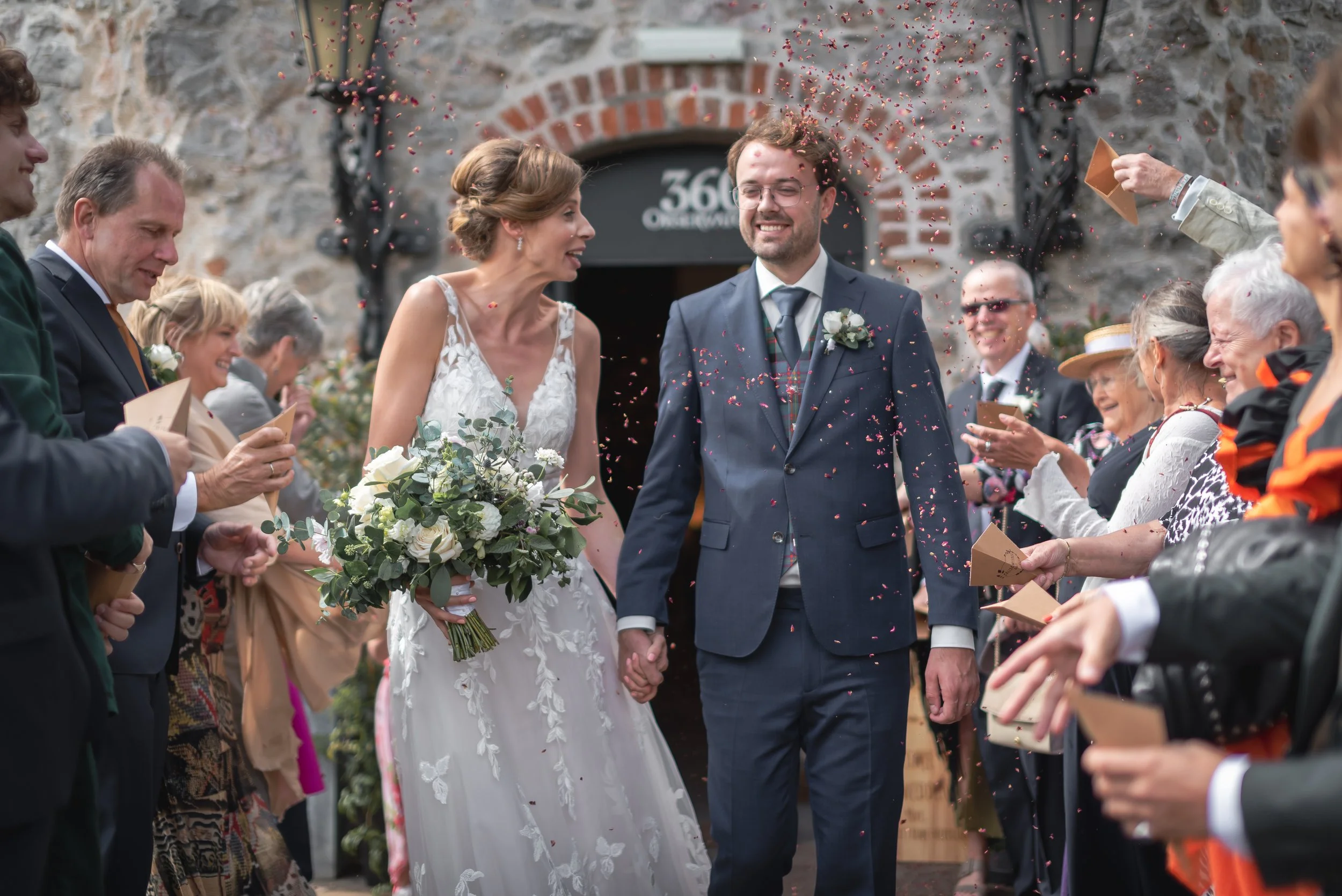 Bride and groom walking through a colourful confetti throw surrounded by guests at Clifton Observatory wedding.